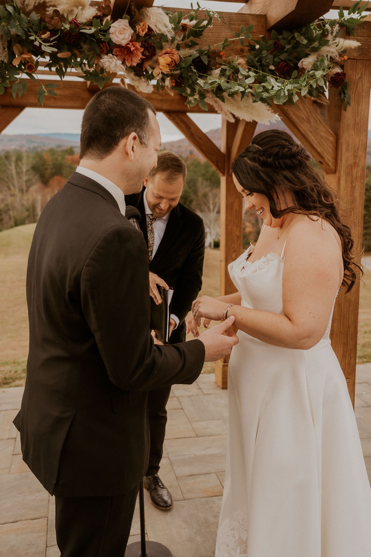An intimate wedding ceremony moment as a couple exchanges rings under a rustic wooden arch.