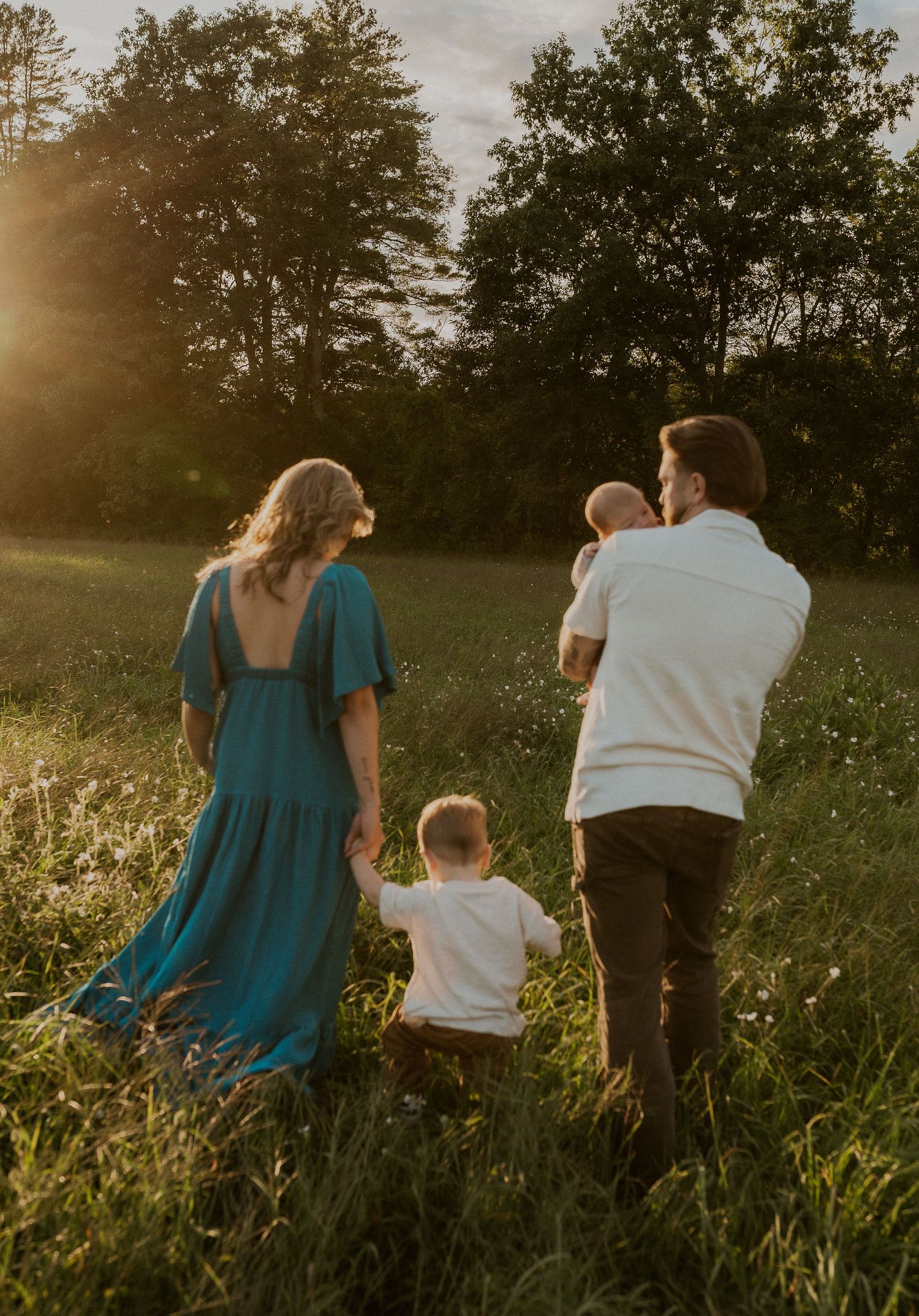 Family walking together through tall grass during golden hour.