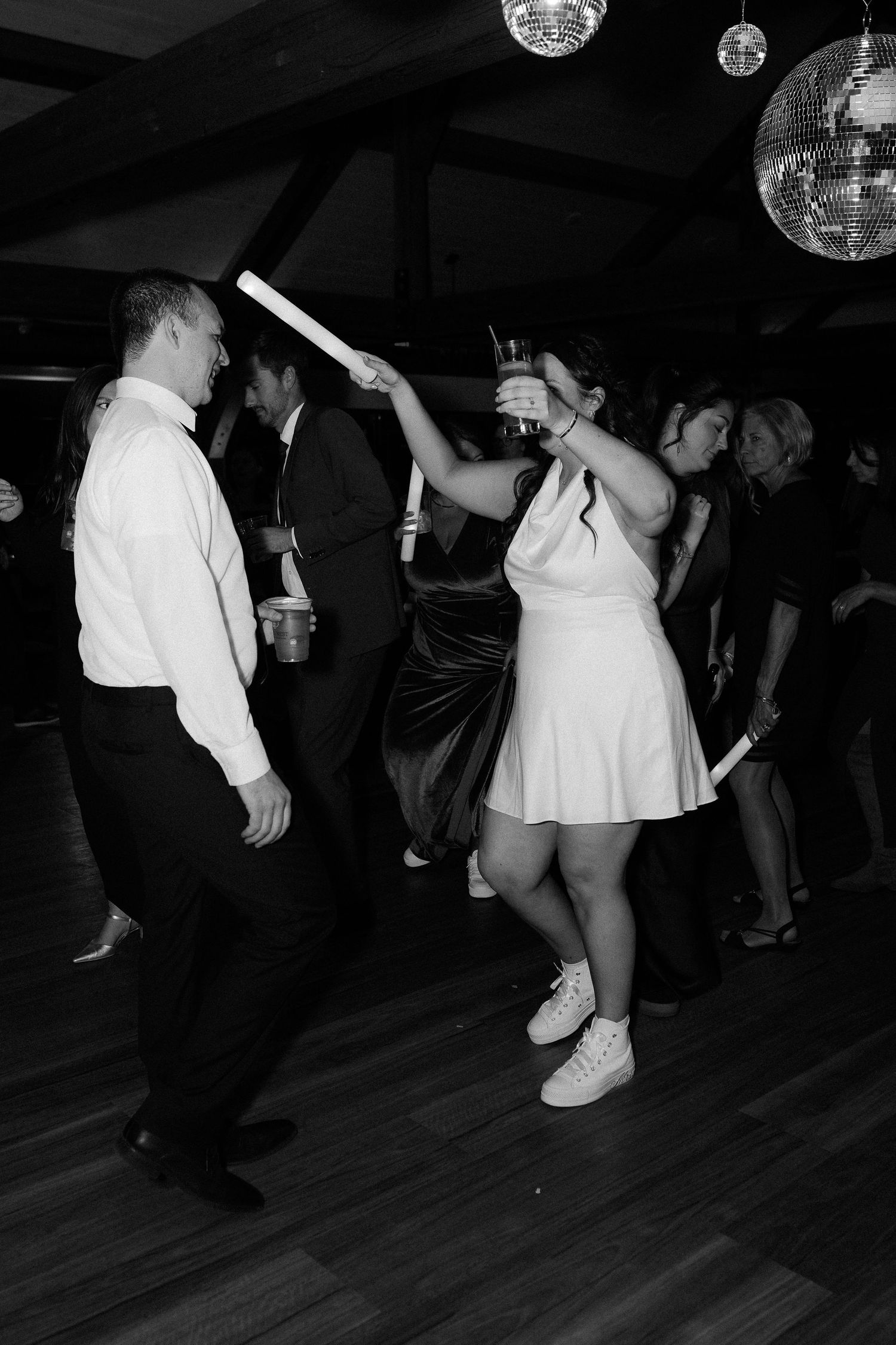 Black and white photos of people dancing under disco balls at a wedding reception on a wooden dance floor.