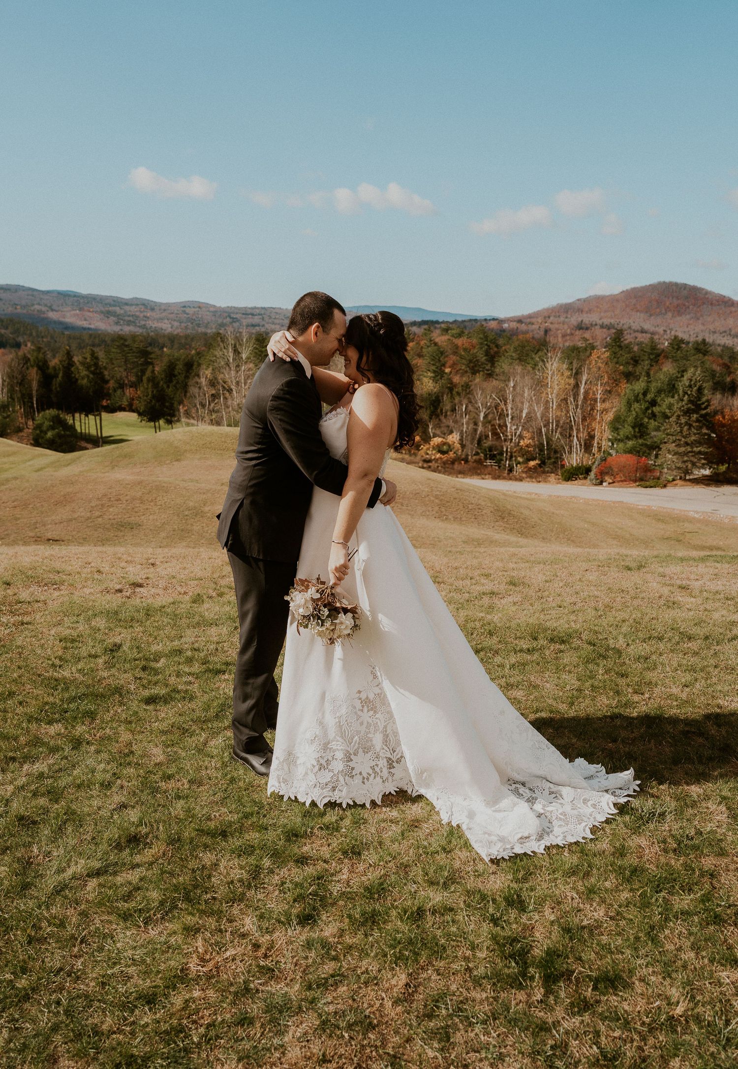 A wedding couple shares an intimate dip while dancing outdoors against a mountainous autumn landscape.