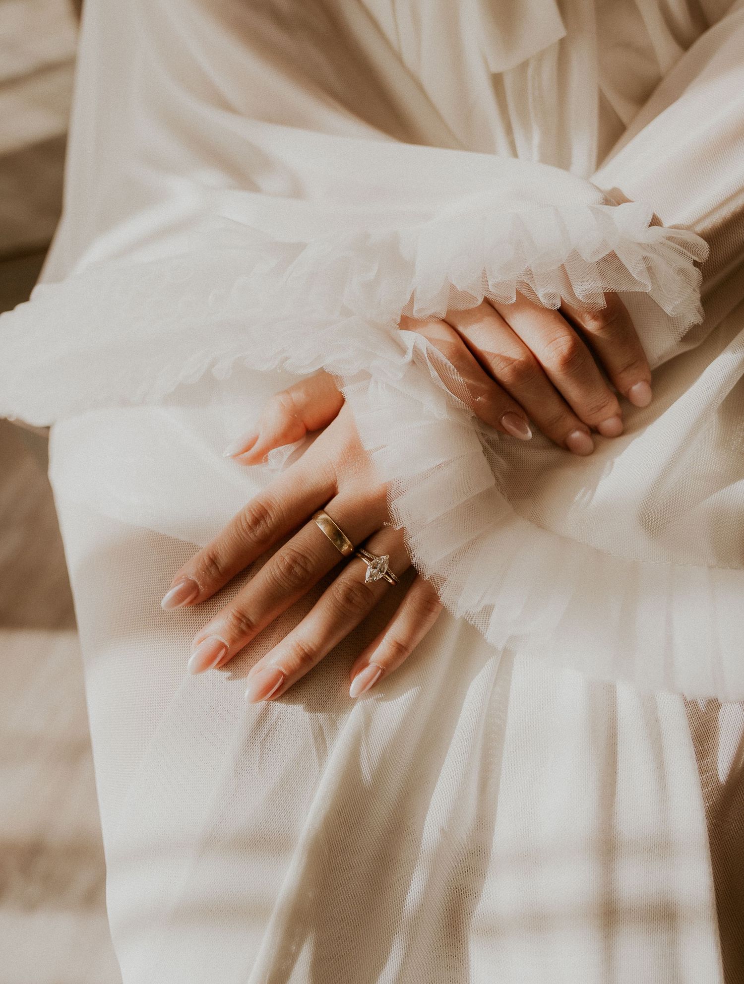 Close-up details of delicate white wedding dress fabric with hands showing an engagement ring.