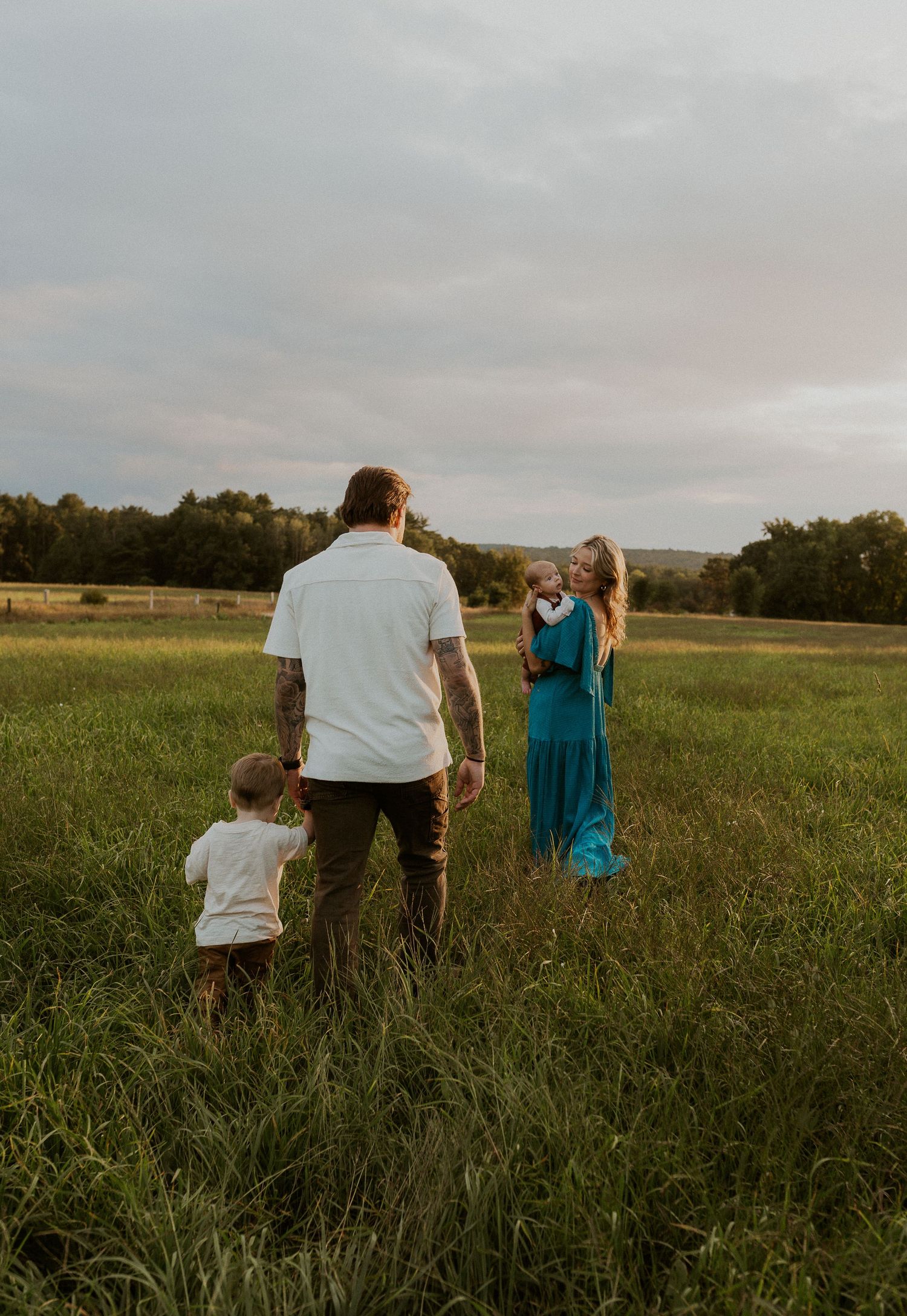 Family standing in meadow during golden hour with dramatic sky.