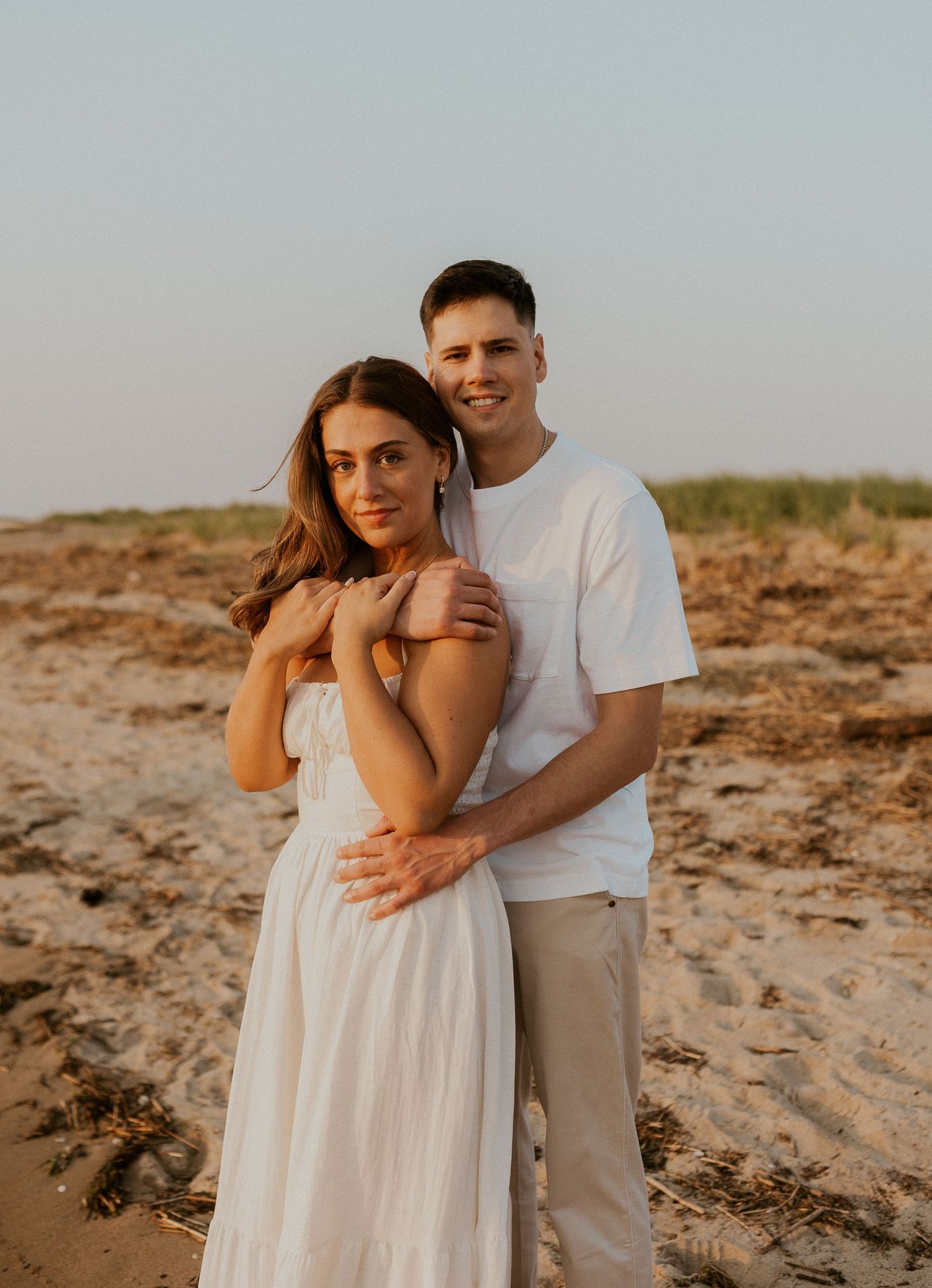 Romantic beach photoshoot of a couple in white and beige attire during golden hour.