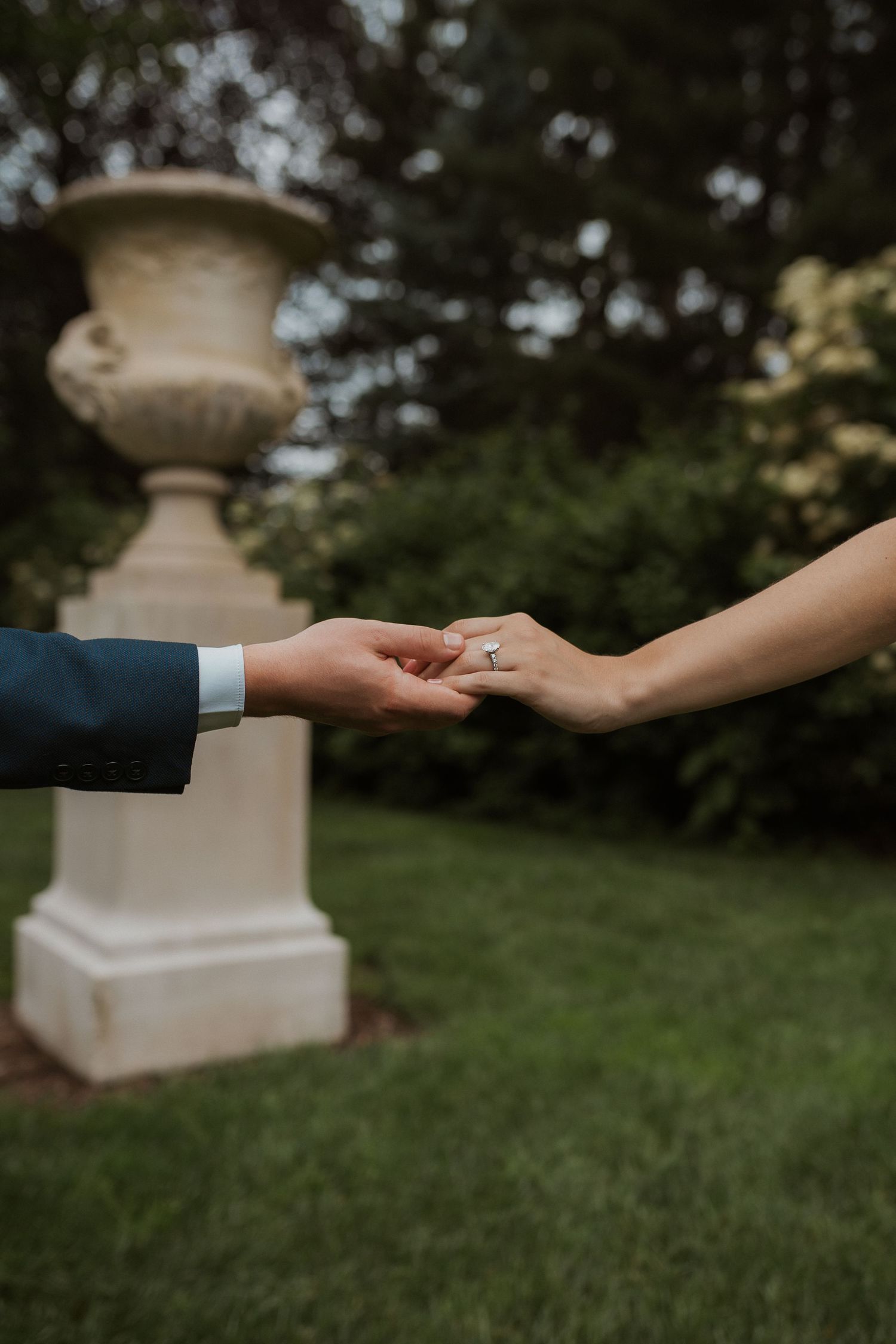 Two hands reaching out to each other against a blurred garden background with decorative stone pillars.