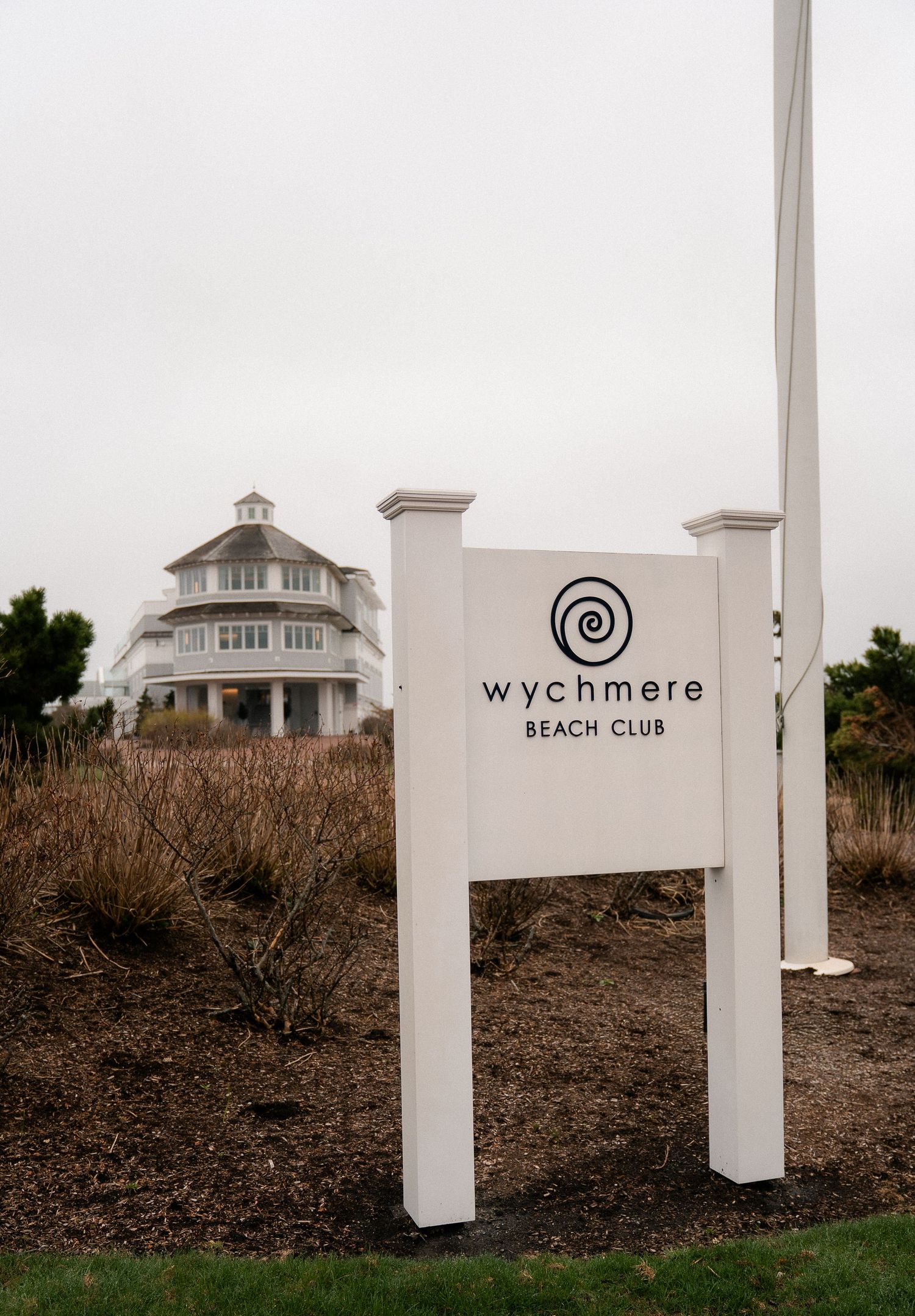 White sign for Wychmere Beach Club stands before a elegant shingled clubhouse on an overcast day.