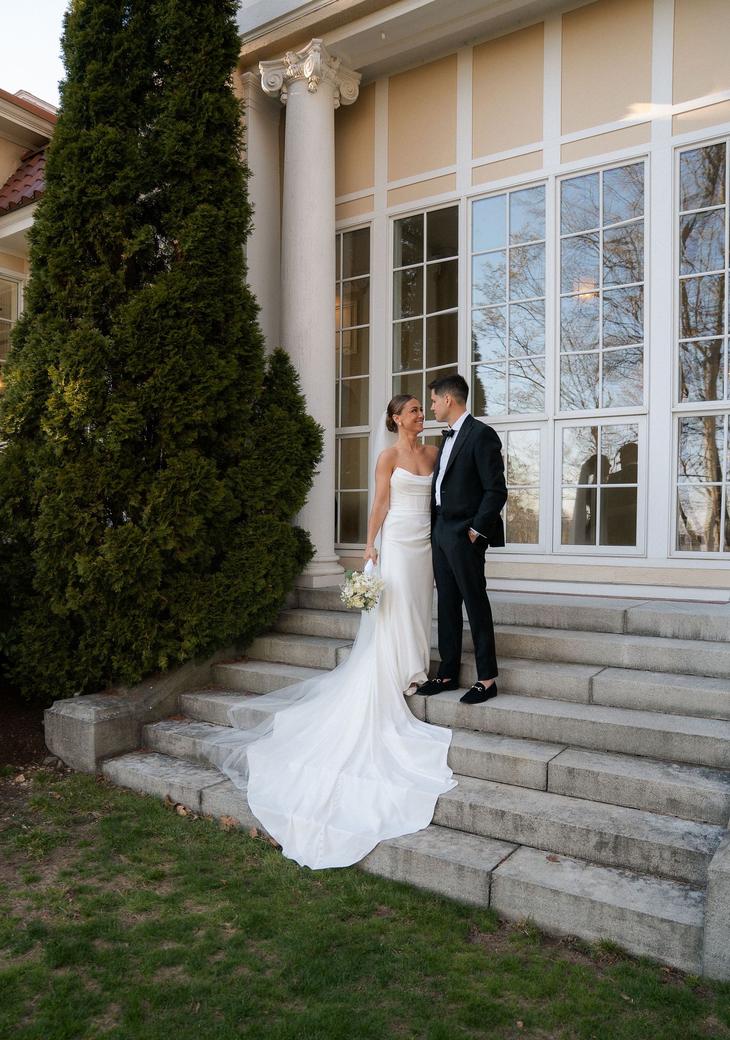 Bride and groom share a romantic moment on elegant stone steps outside a classic venue with tall columns.