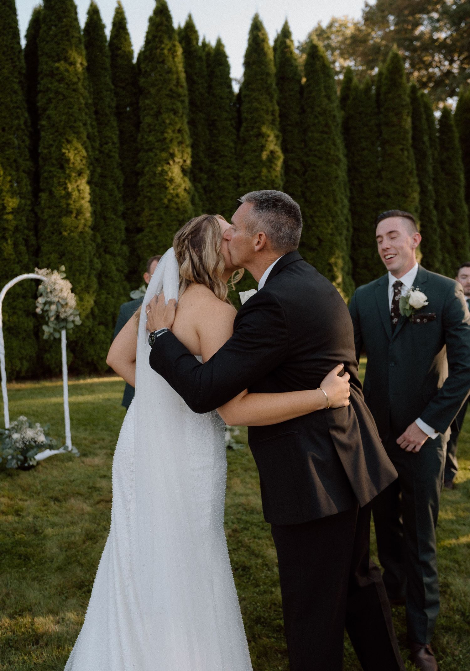 Touching father-daughter wedding moment in front of tall cypress trees during golden hour.