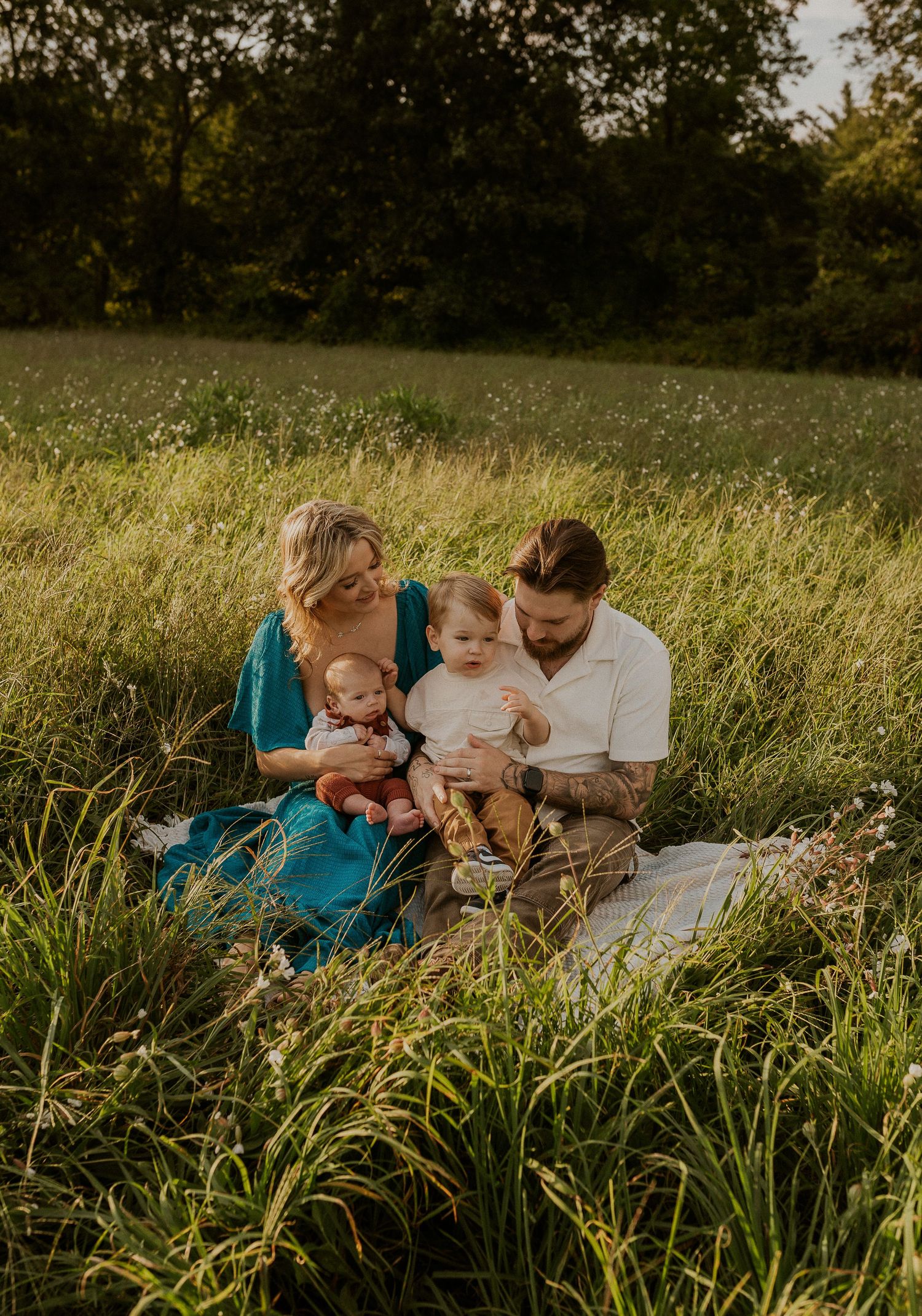Family lounging together in a sunny meadow filled with tall grass and wildflowers.