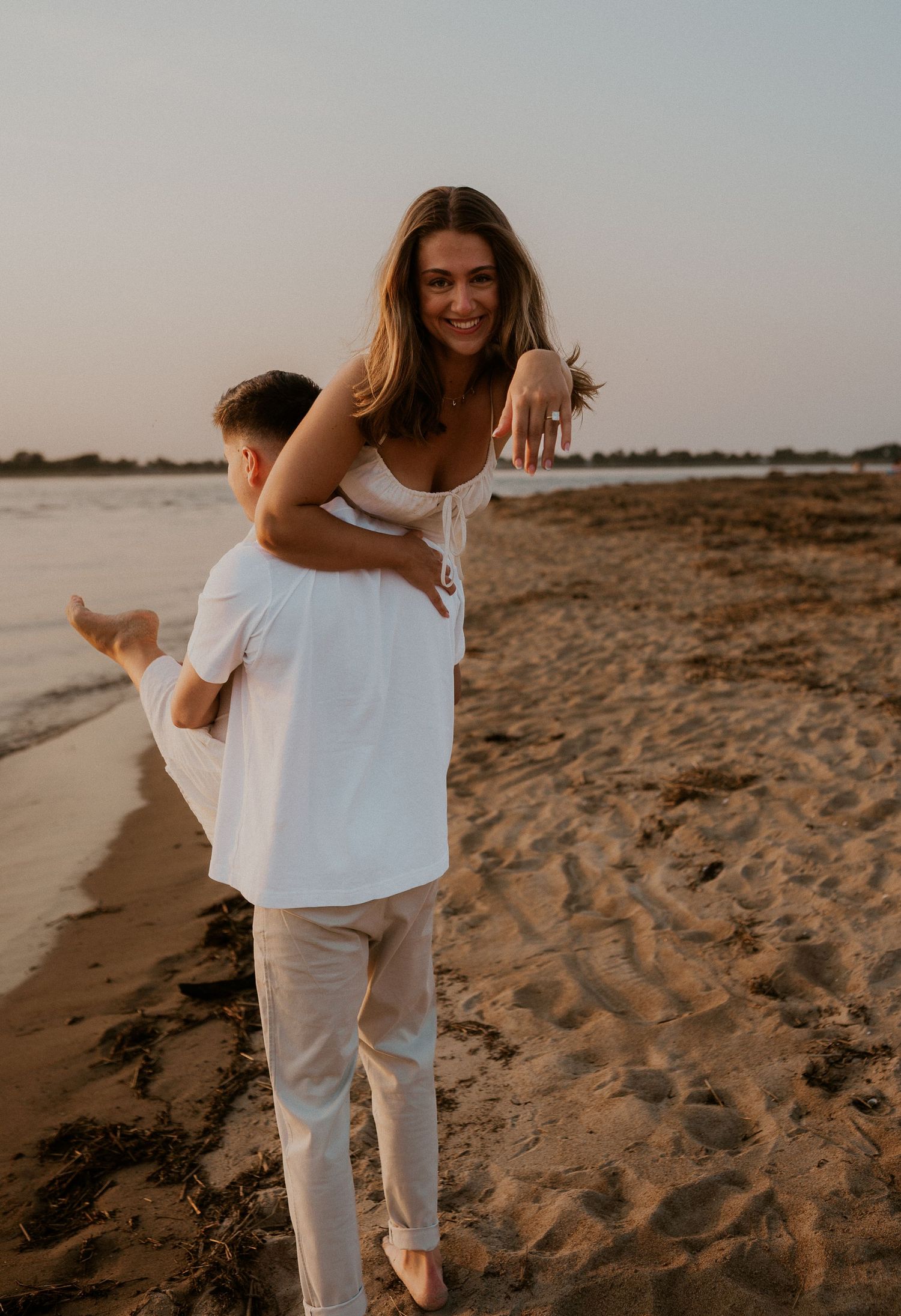 Joyful couple having fun with piggyback rides on sandy beach during golden hour.