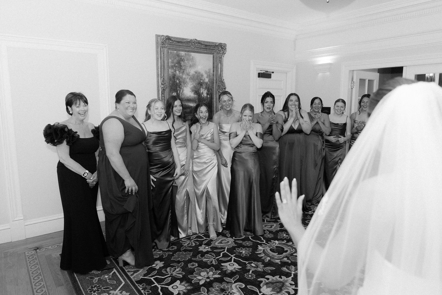 Black and white photo of bridesmaids reacting emotionally to bride's first look reveal at elegant venue.