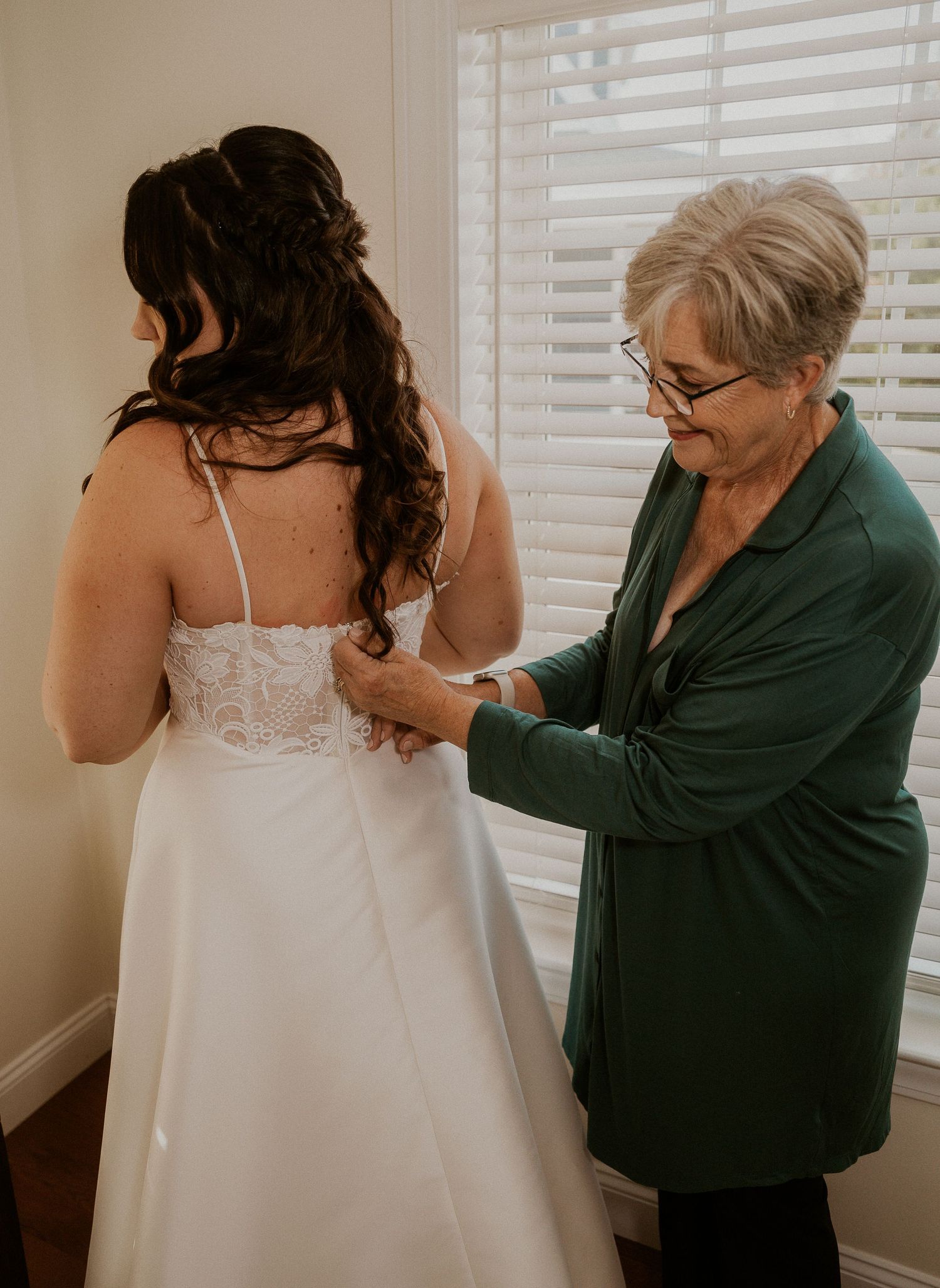 A sequence of photos showing someone helping another person put on a white wedding dress near a window.