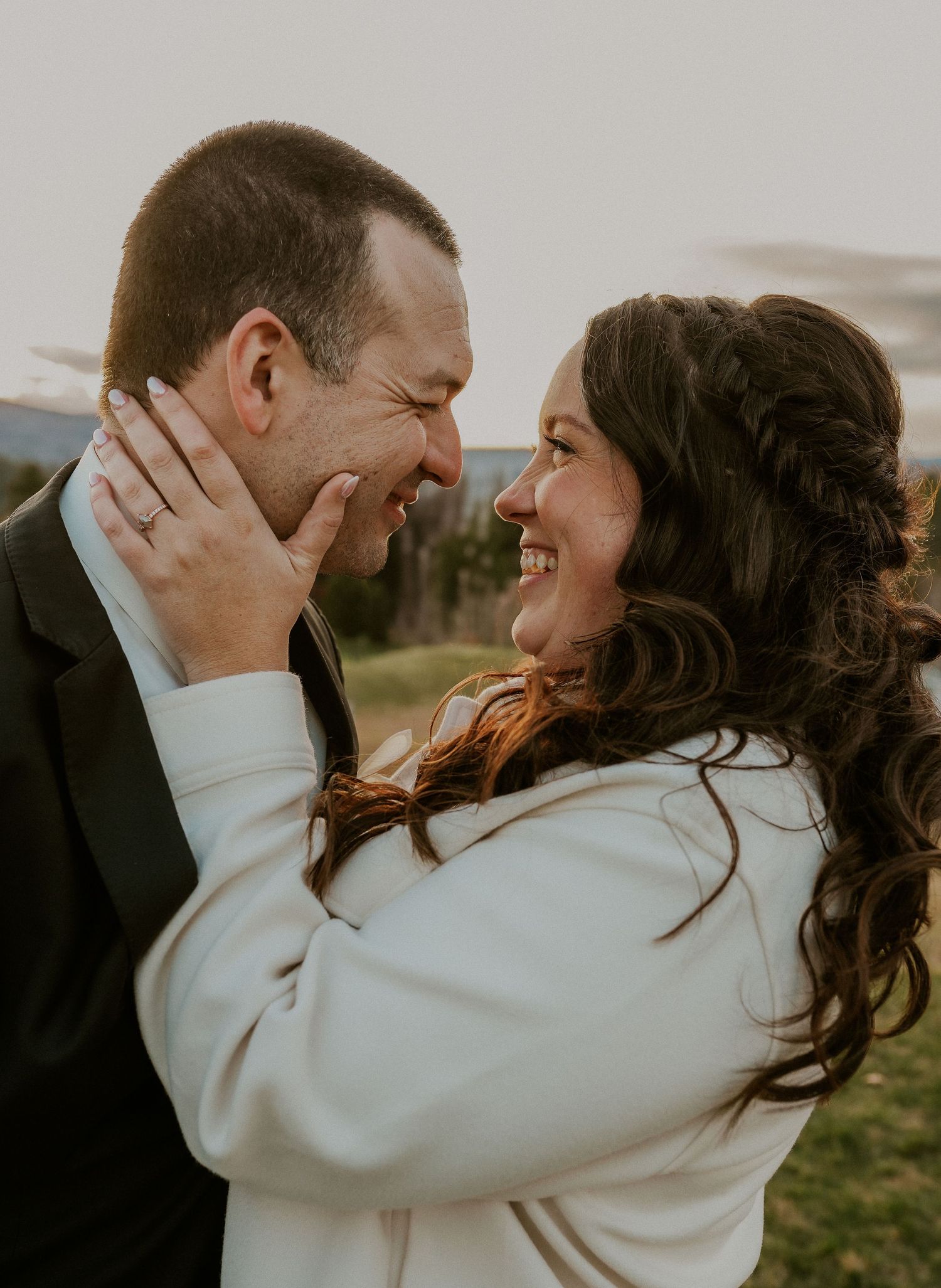 A romantic couple embracing and laughing together outdoors during a sunset photoshoot.