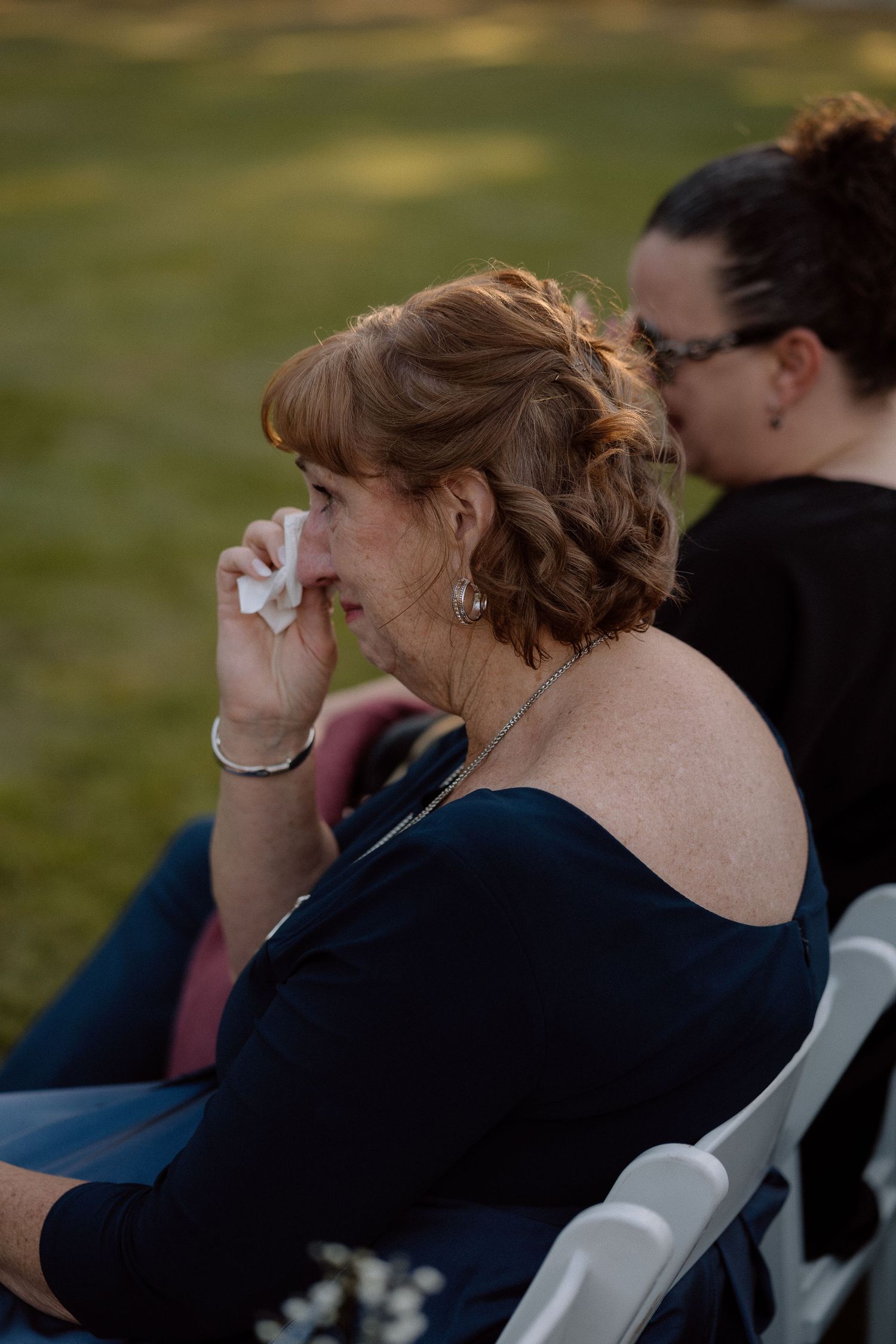 Wedding guests wiping tears during emotional outdoor ceremony moment.