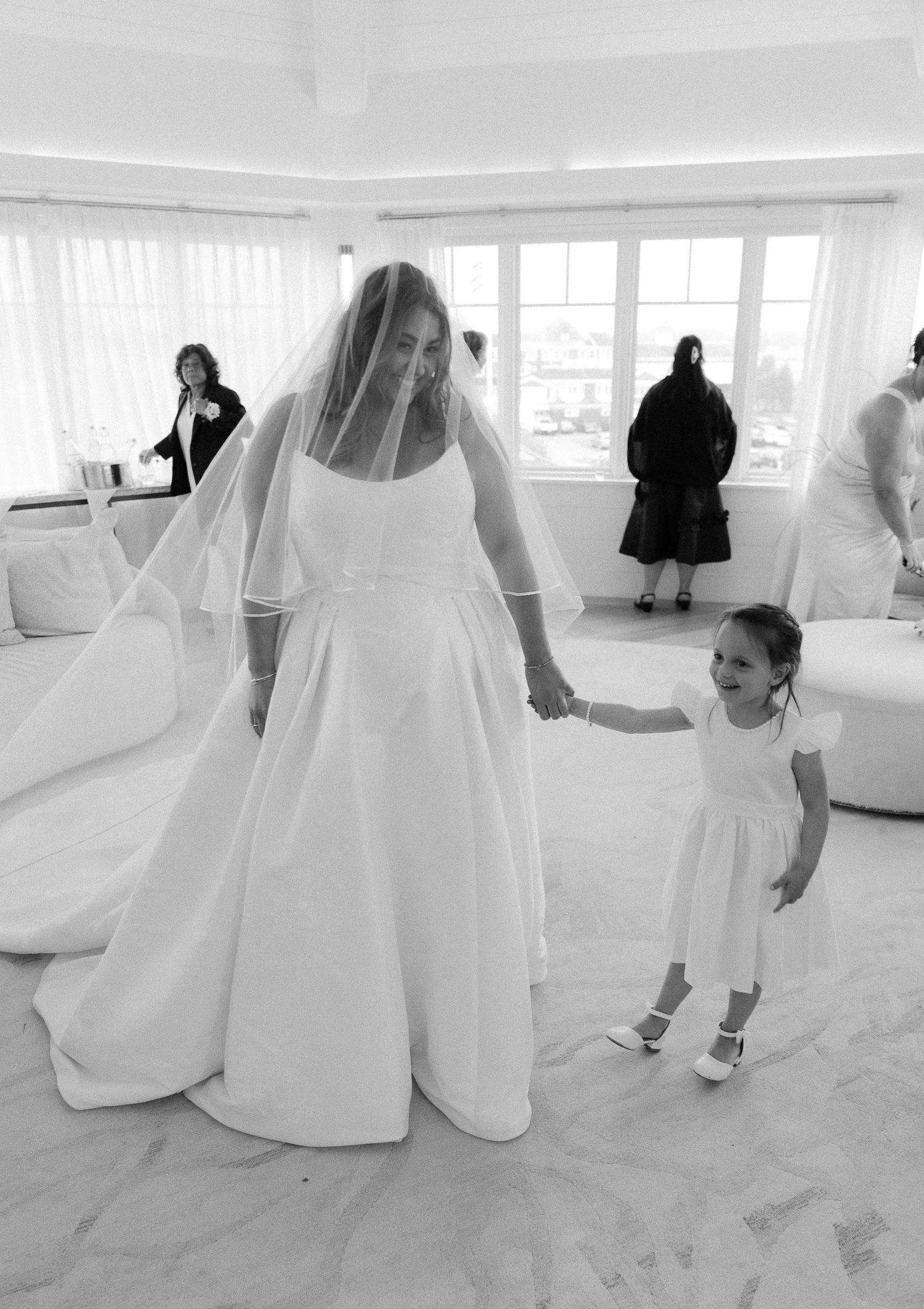 Black and white photo of bride in ball gown and veil holding hands with flower girl in white dress.