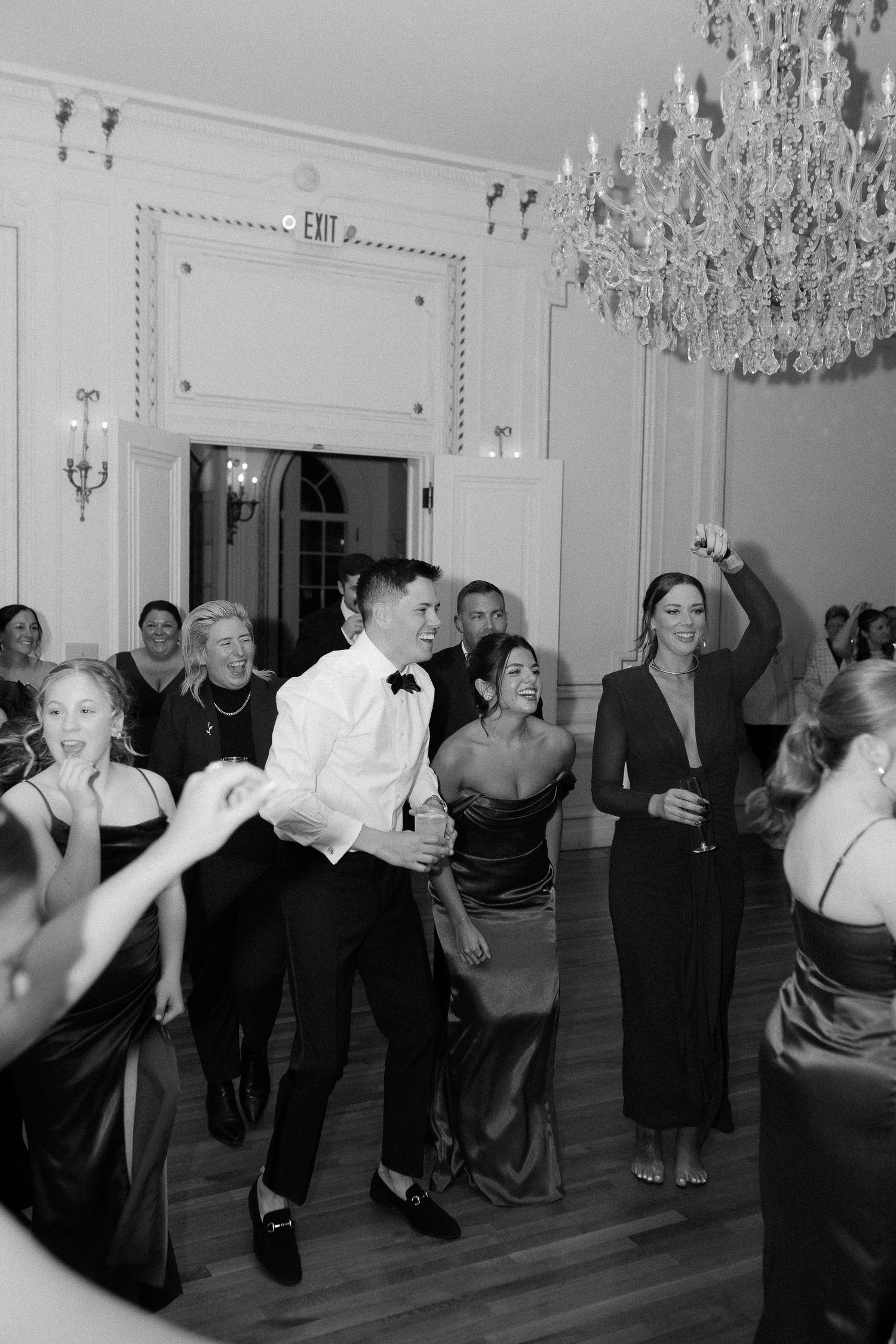 Guests dancing joyfully at an elegant wedding reception in a grand ballroom with crystal chandeliers.
