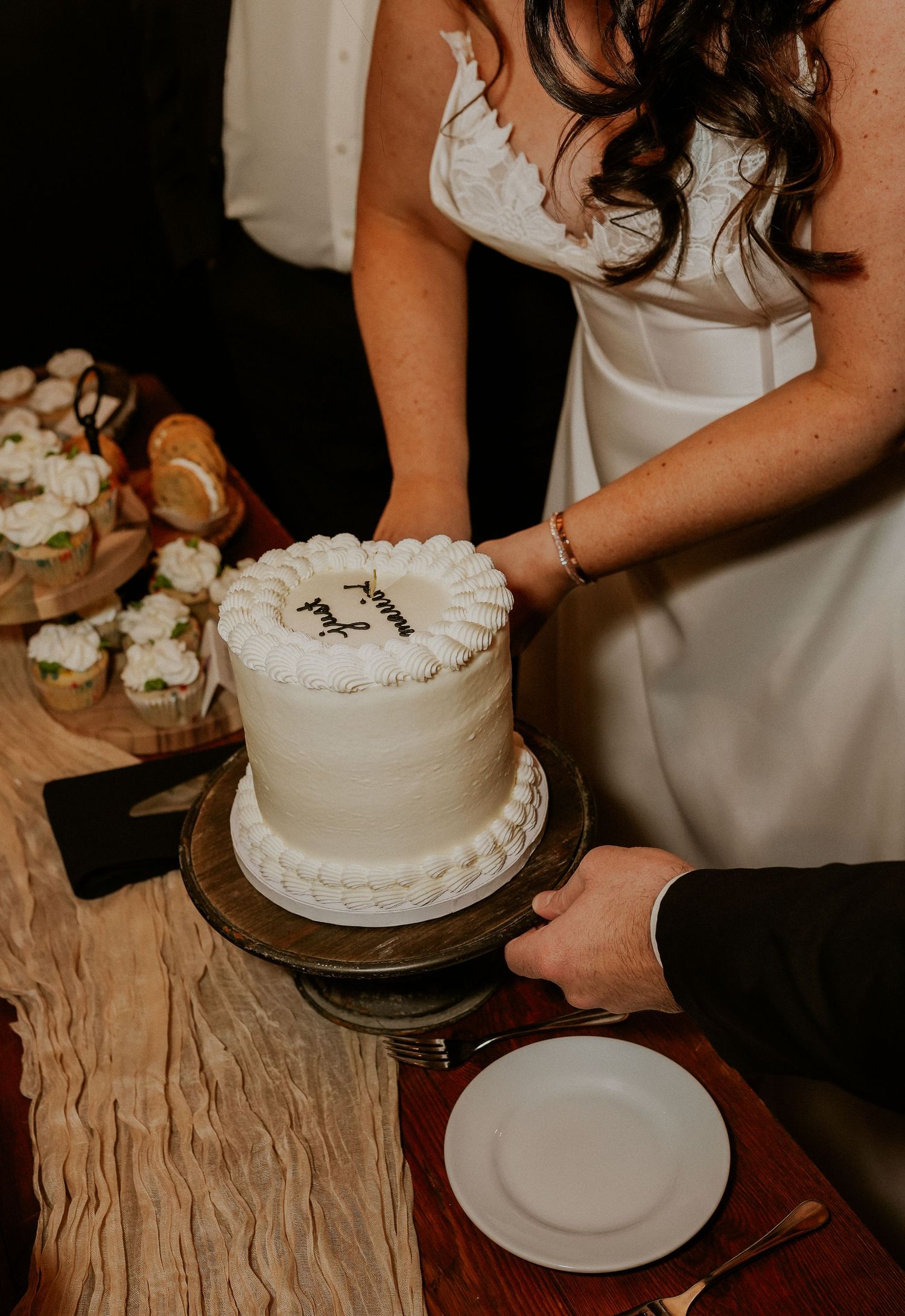 A white wedding cake being cut on a rustic wooden table with floral decorations.