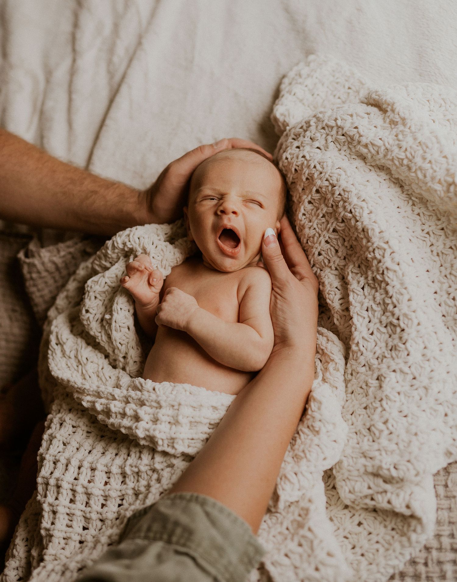 Baby lying on soft knitted blanket with hands reaching to touch.