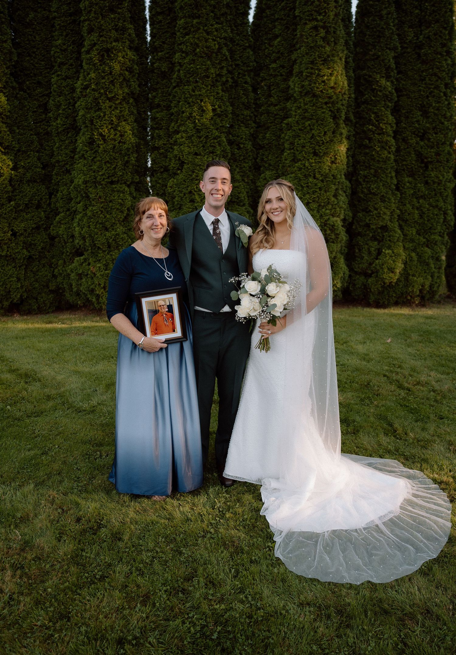 Wedding portrait against tall evergreen hedges with a flowing white bridal gown and veil.