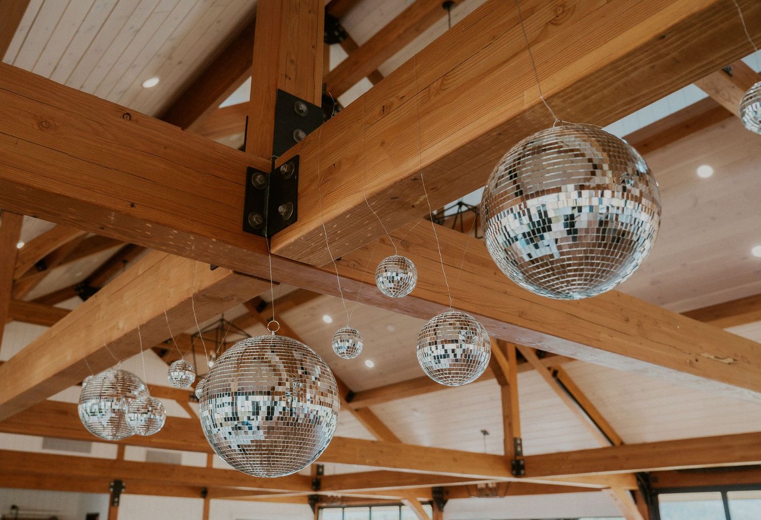 Wooden beamed ceiling with multiple disco balls hanging in a rustic venue space.