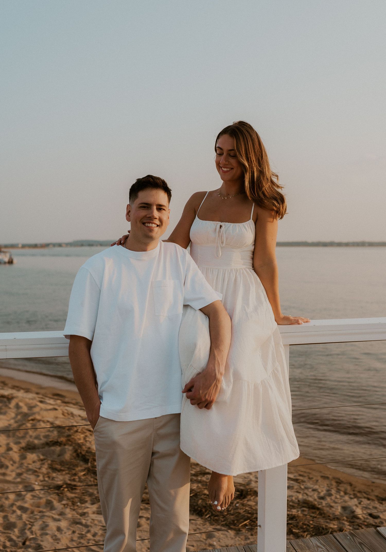 A couple holding hands while standing on a coastal dock during golden hour.