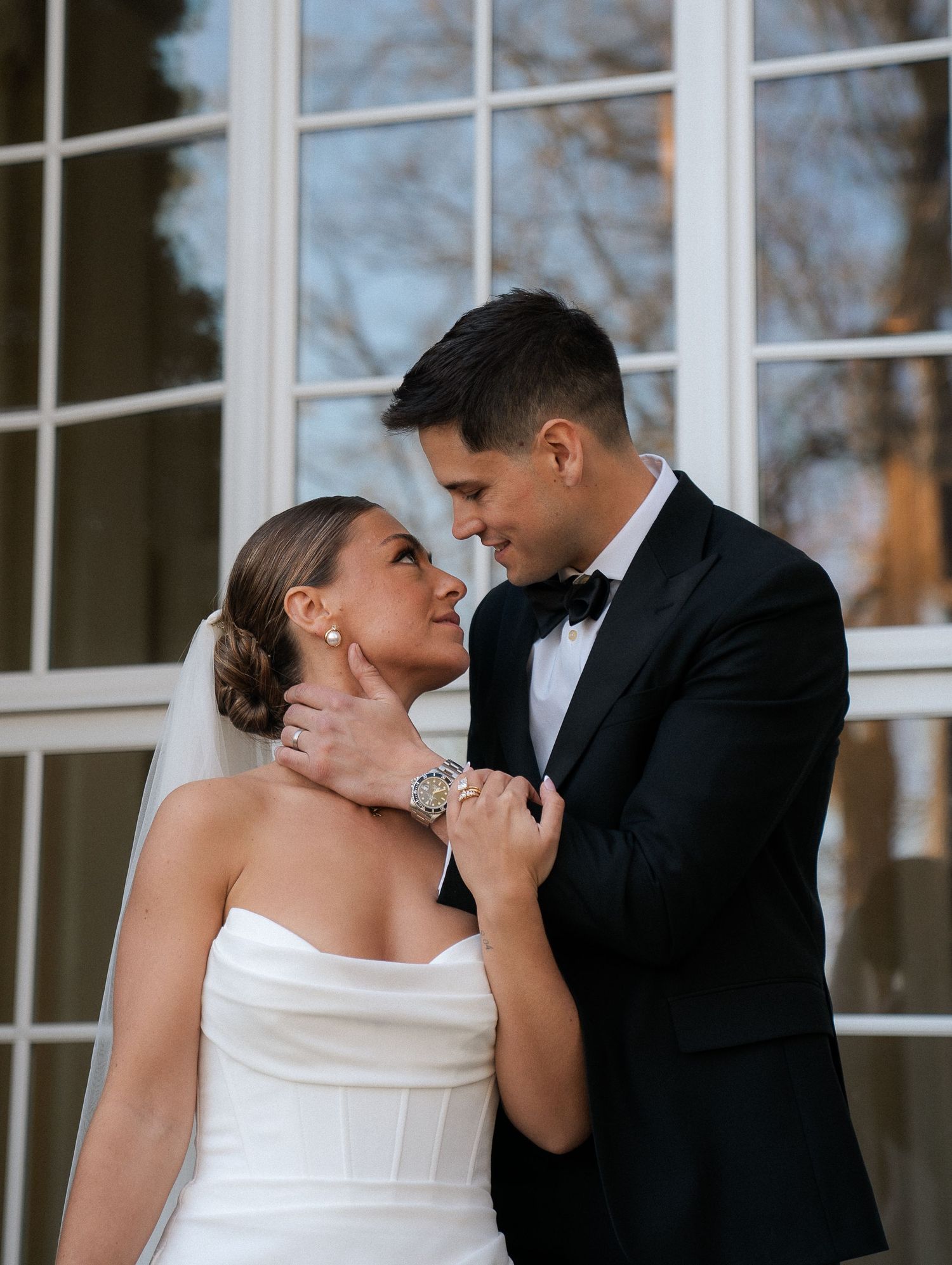 Bride in strapless white gown and groom in black tuxedo share an intimate gaze during wedding portraits.