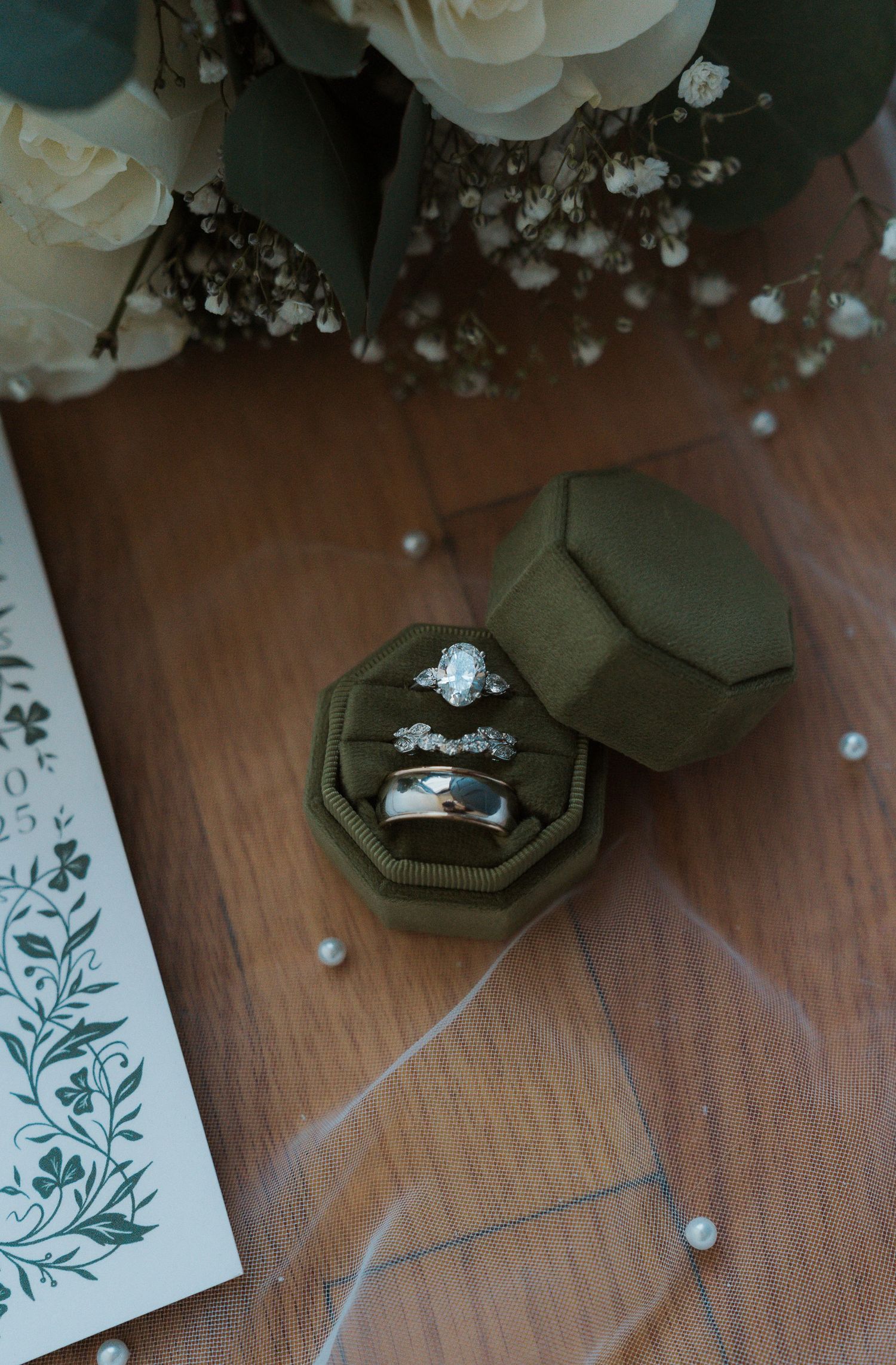 Elegant wedding details featuring rings, invitations, and white roses on wooden surface.