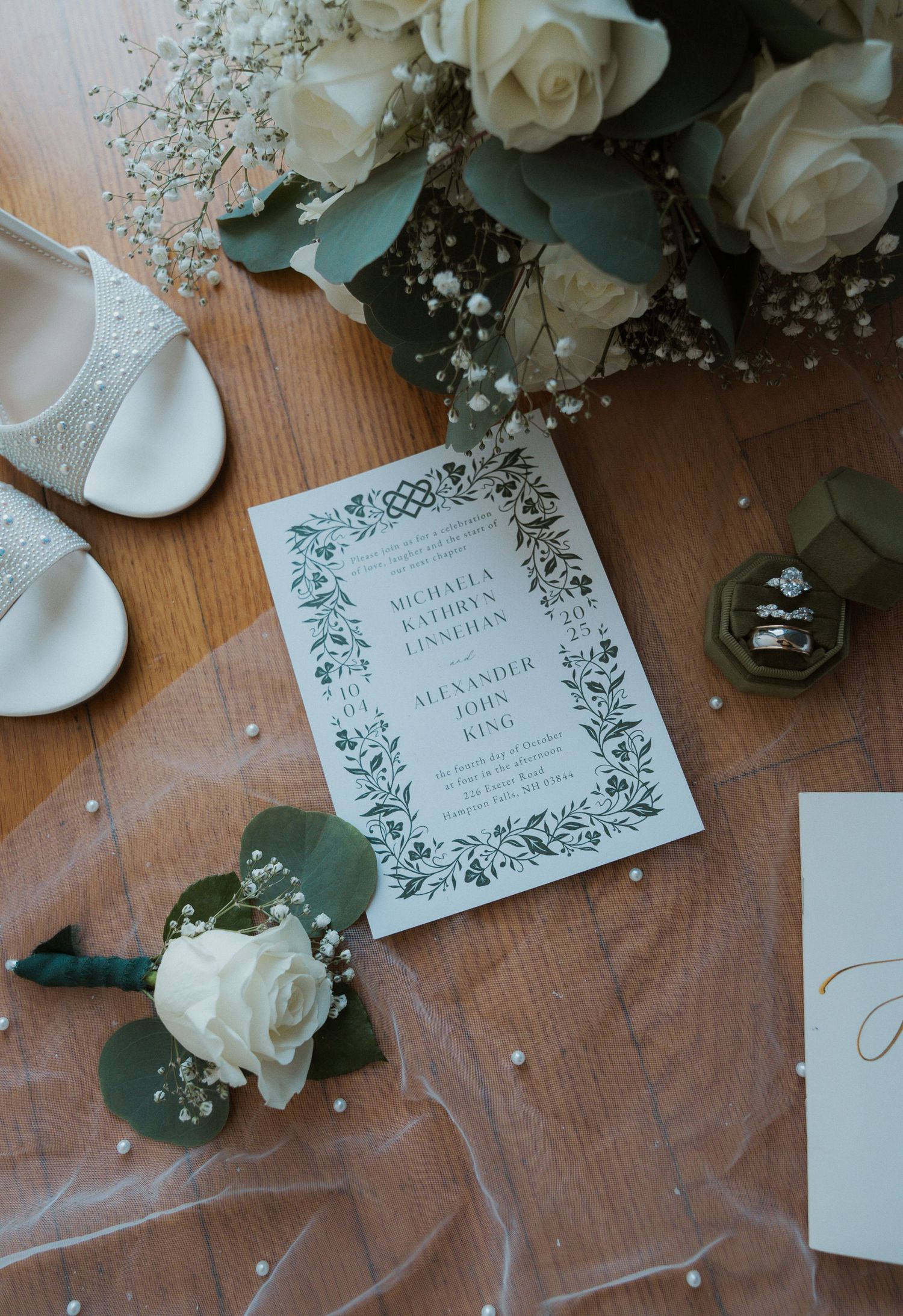 Wedding stationery flatlay with white roses, greenery and elegant floral-bordered invitation.