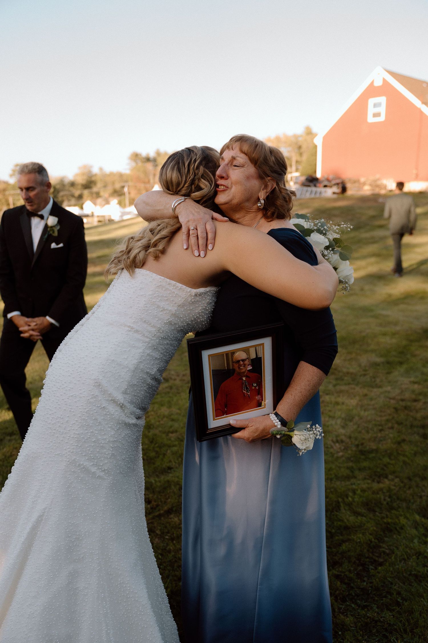An emotional embrace during an outdoor wedding ceremony with a red barn in the background.