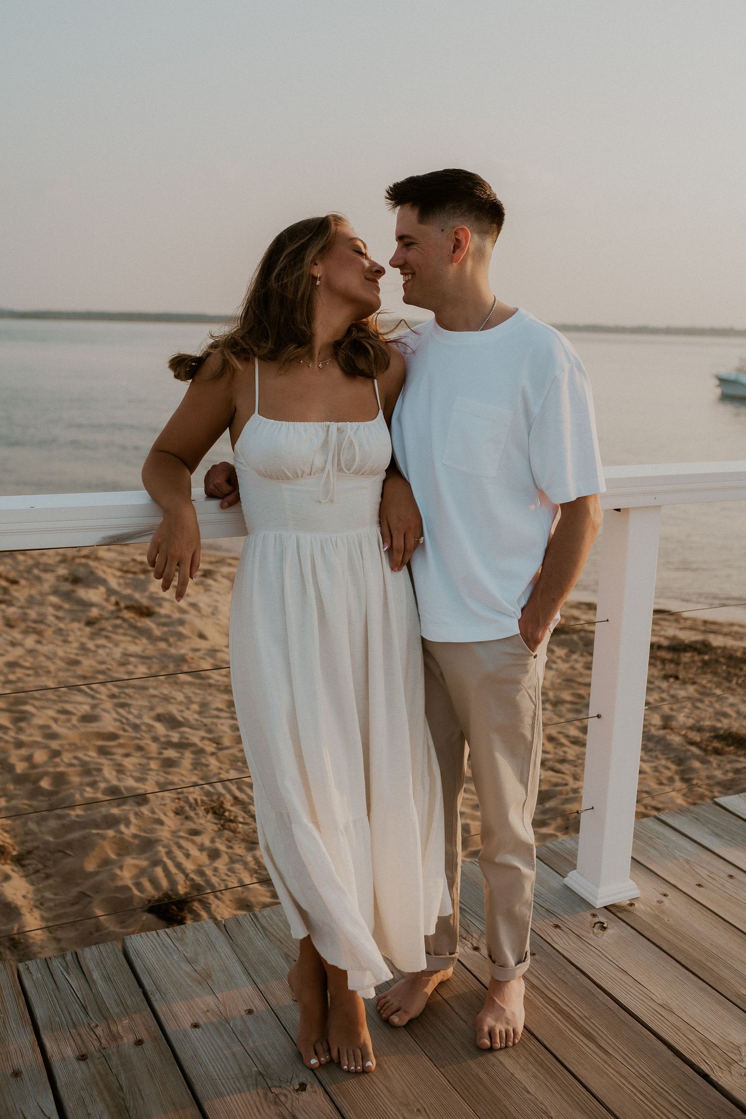Couple sharing romantic moment on wooden boardwalk by the beach at sunset.