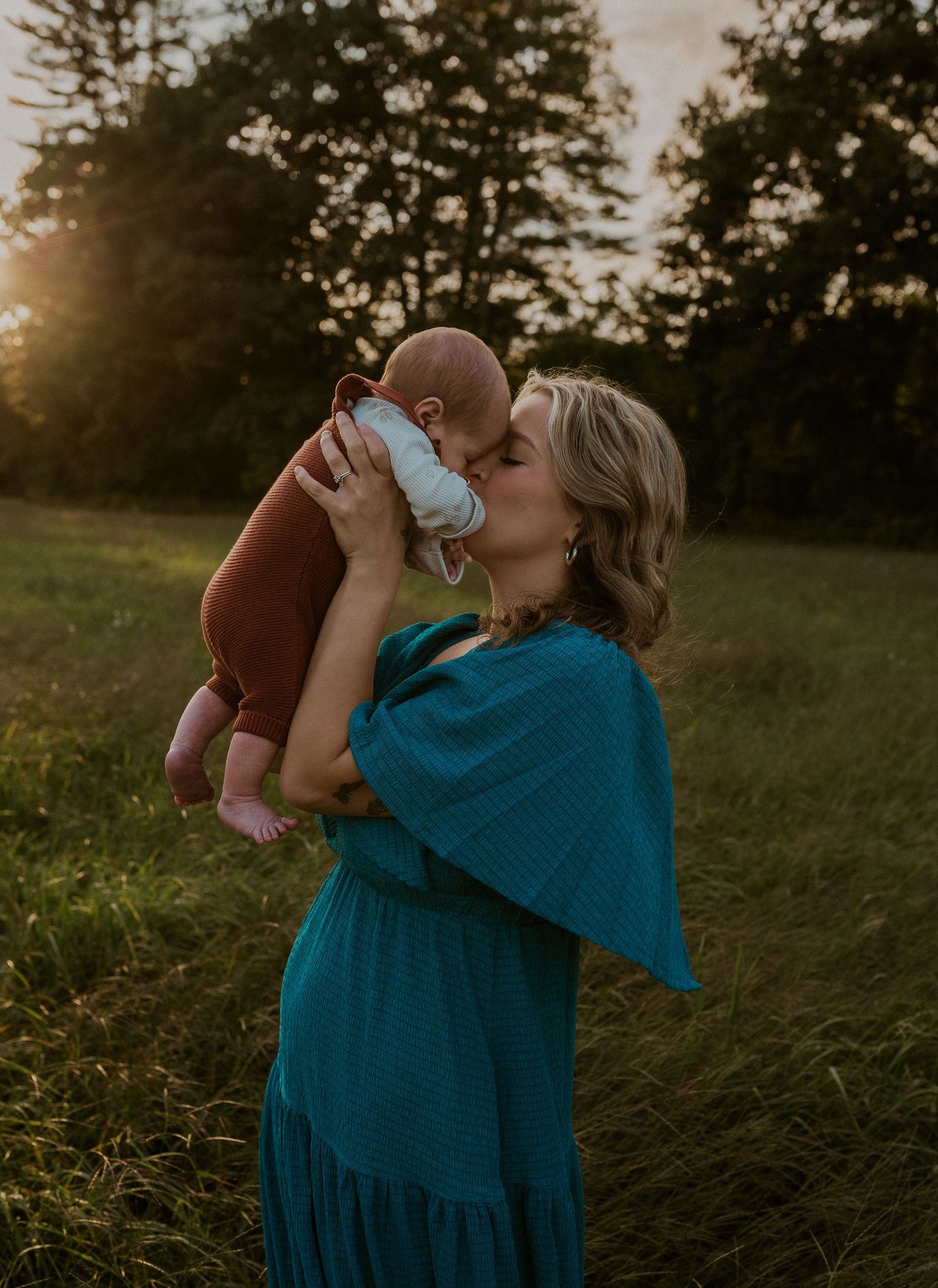 Person in teal dress embraces lovingly in a sunset-lit field.