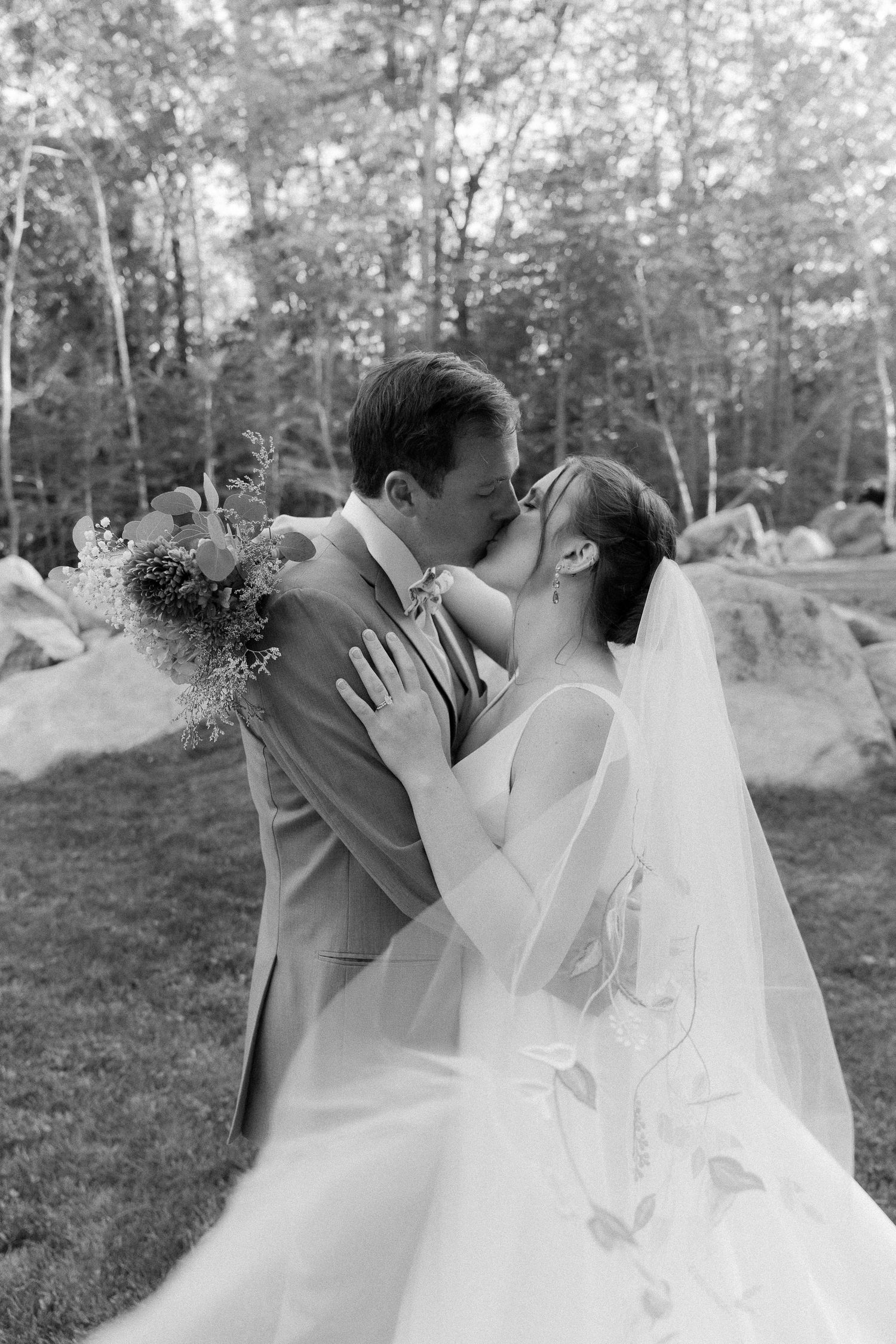 Black and white wedding portrait of couple kissing outdoors among rocks and trees.