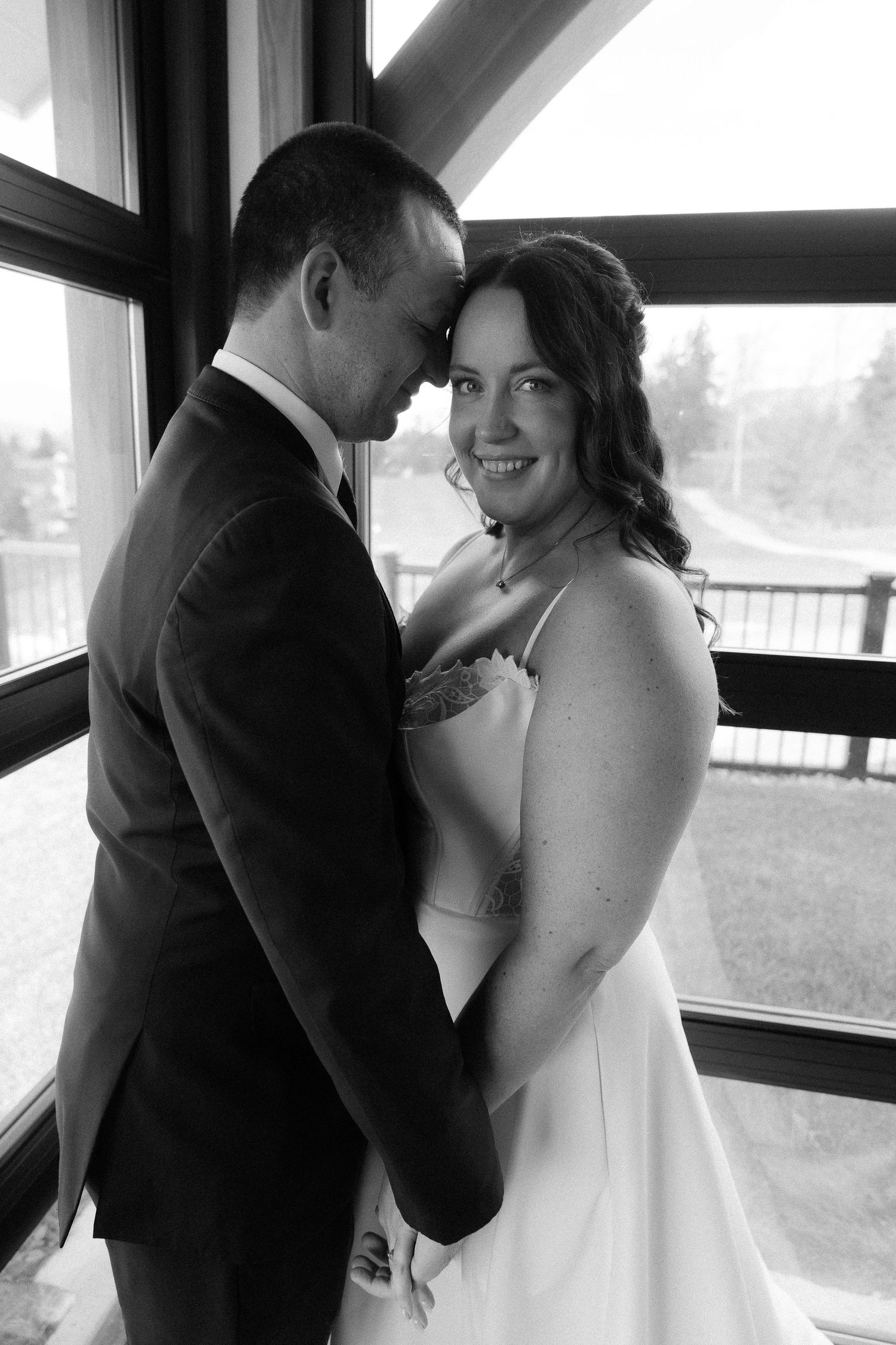 A tender moment between newlyweds is captured in an indoor setting with natural window light.