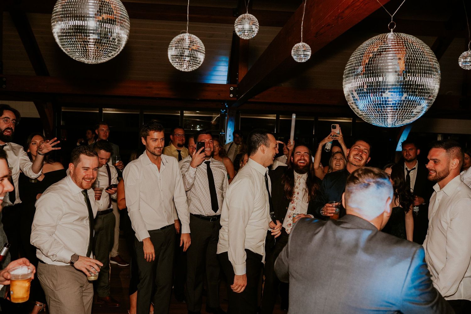 People dancing and celebrating on a dimly lit dance floor with disco balls hanging from the ceiling during a party.