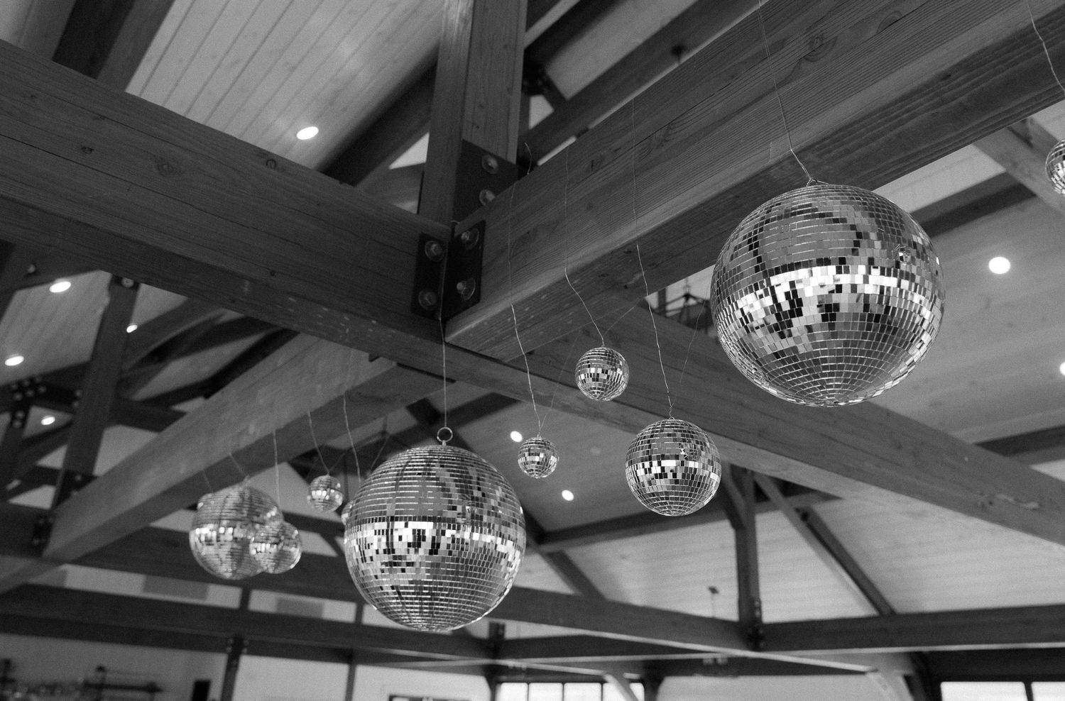 Multiple disco balls hang from dark wooden beams in a black and white interior ceiling shot.
