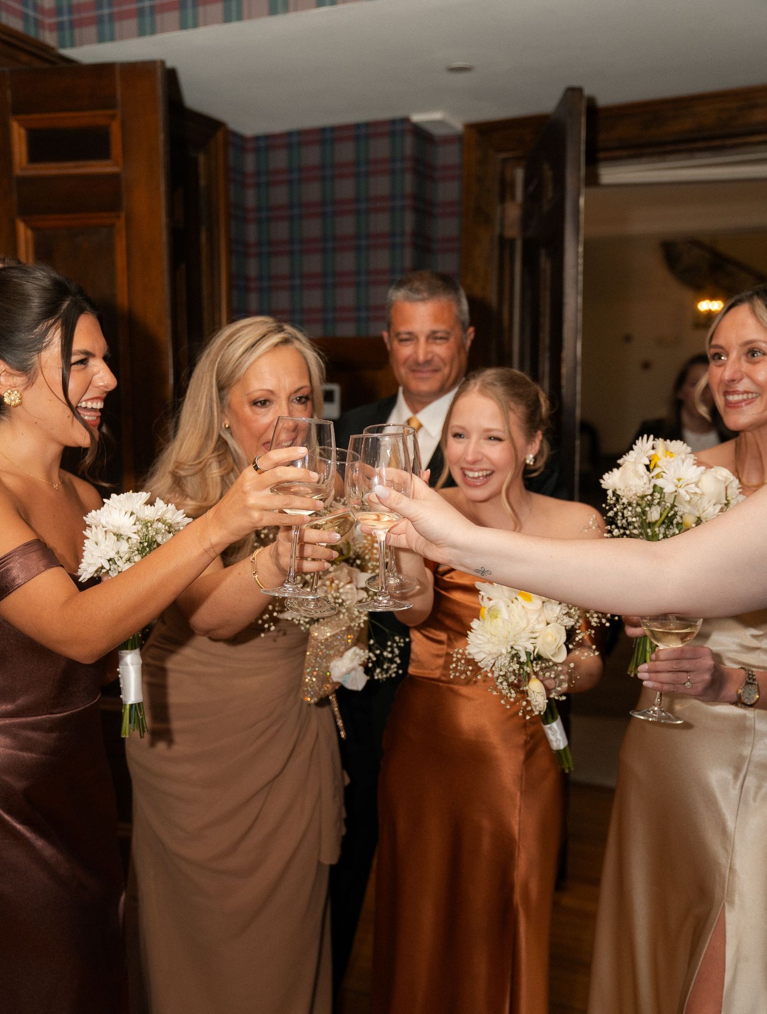 Bridesmaids and wedding guests in earth-tone gowns raise champagne glasses in a joyful celebratory toast.