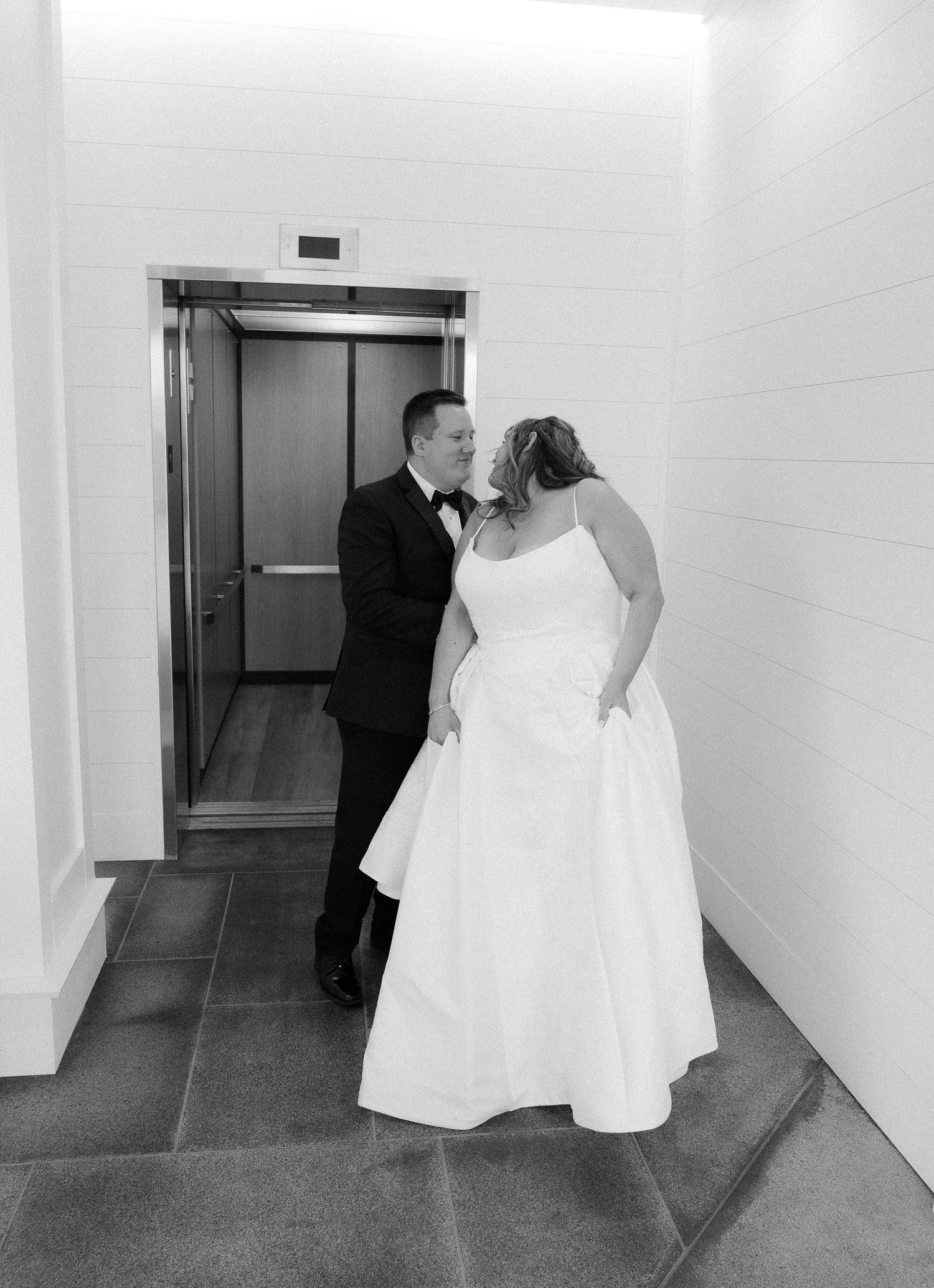 Black and white photo of a bride and groom sharing a kiss near an elevator on their wedding day.