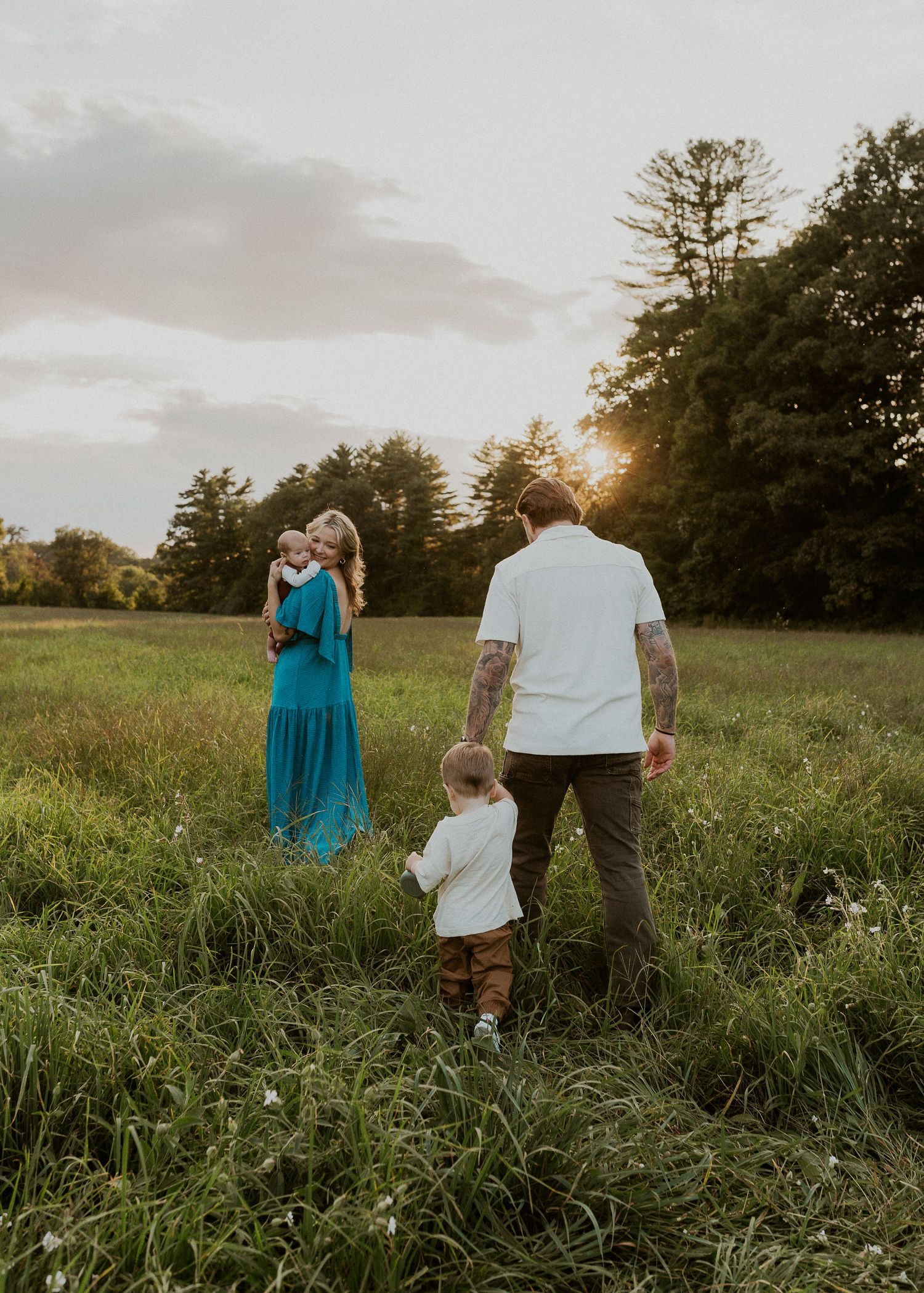 Family enjoying sunset together in tall grass field with trees in background.