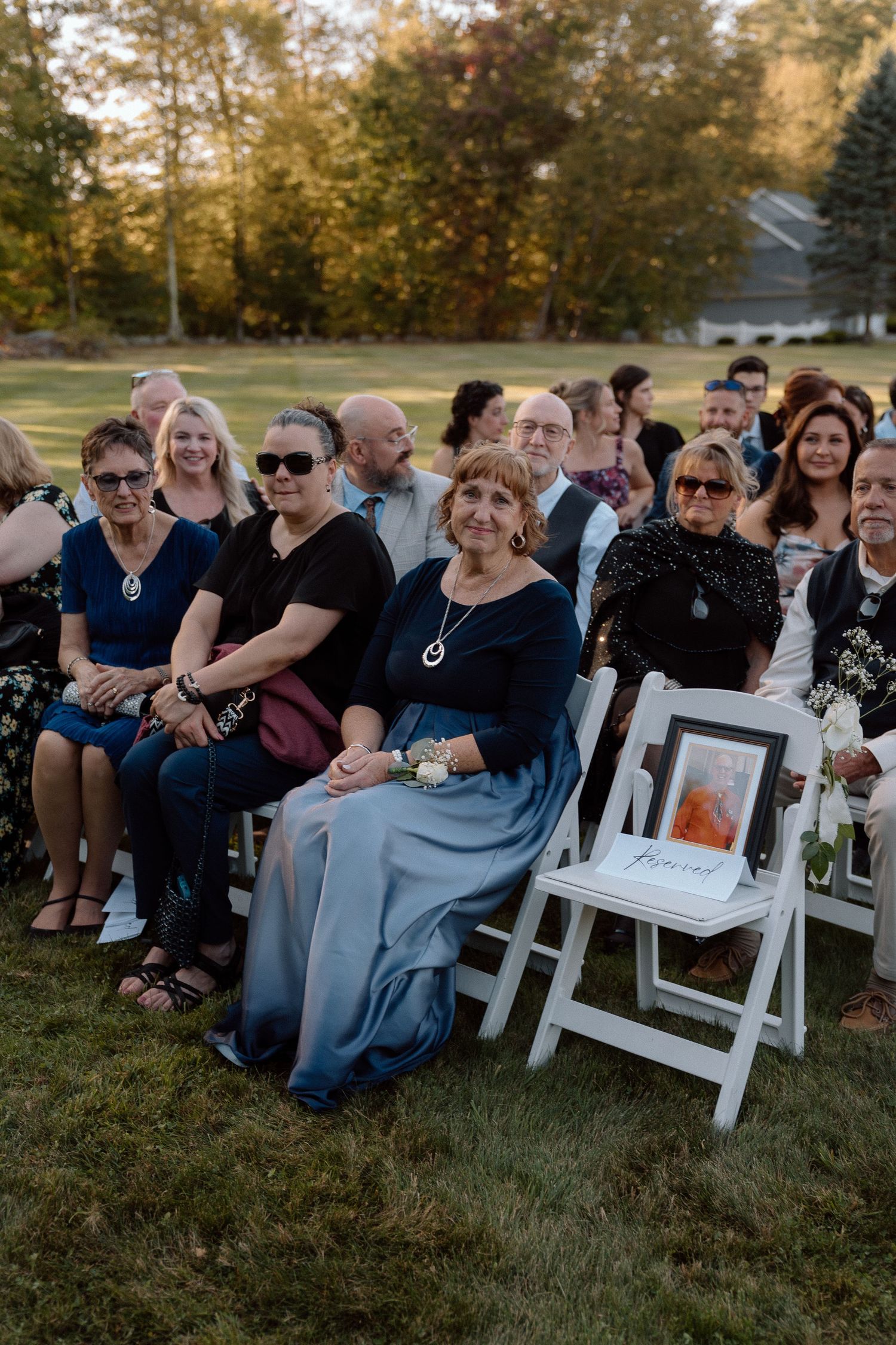 Wedding guests seated in white folding chairs share joyful reactions during an outdoor autumn ceremony.