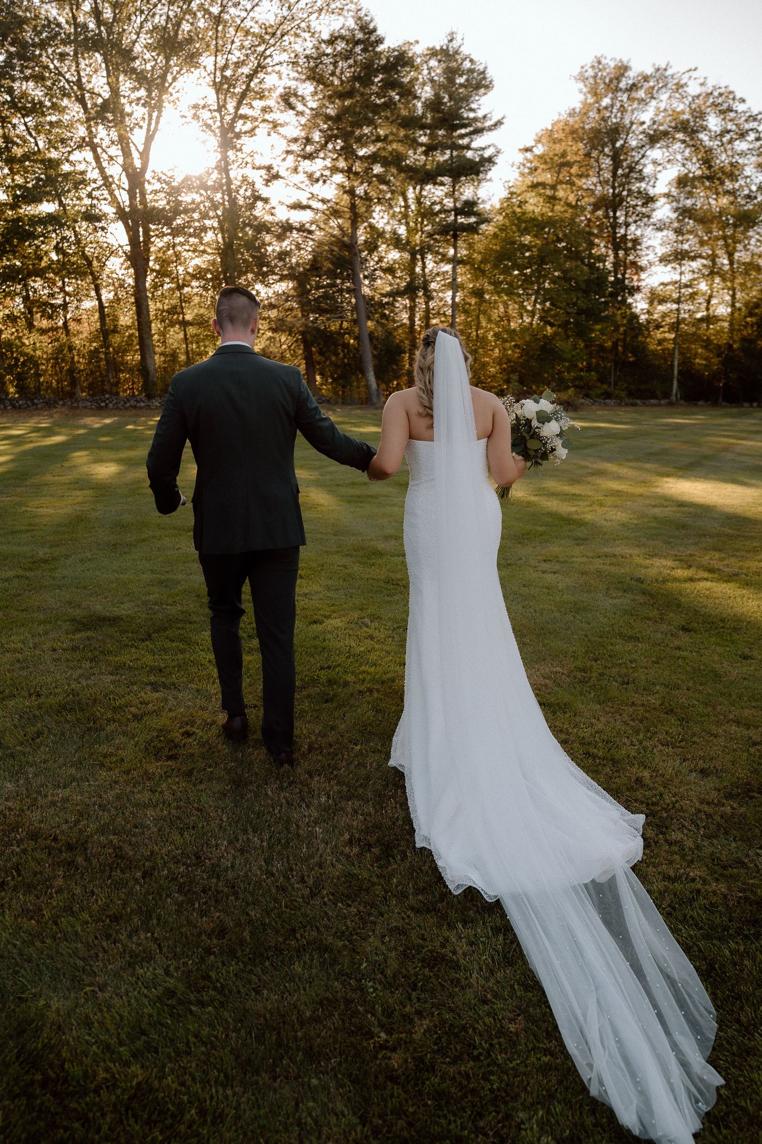 A couple walks through a sunlit field during golden hour at their outdoor wedding.
