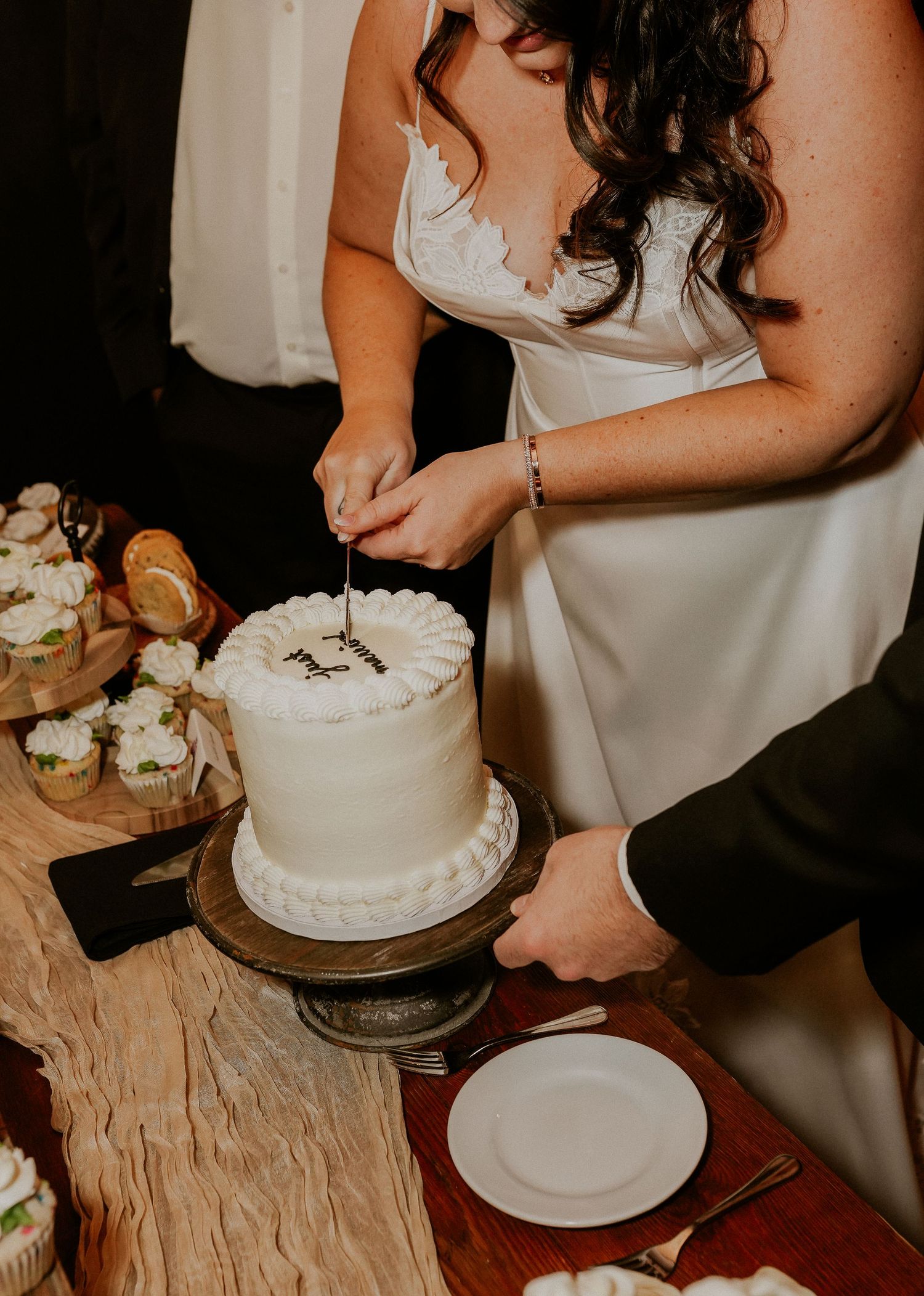 Close-up of hands cutting into a white wedding cake during the reception.
