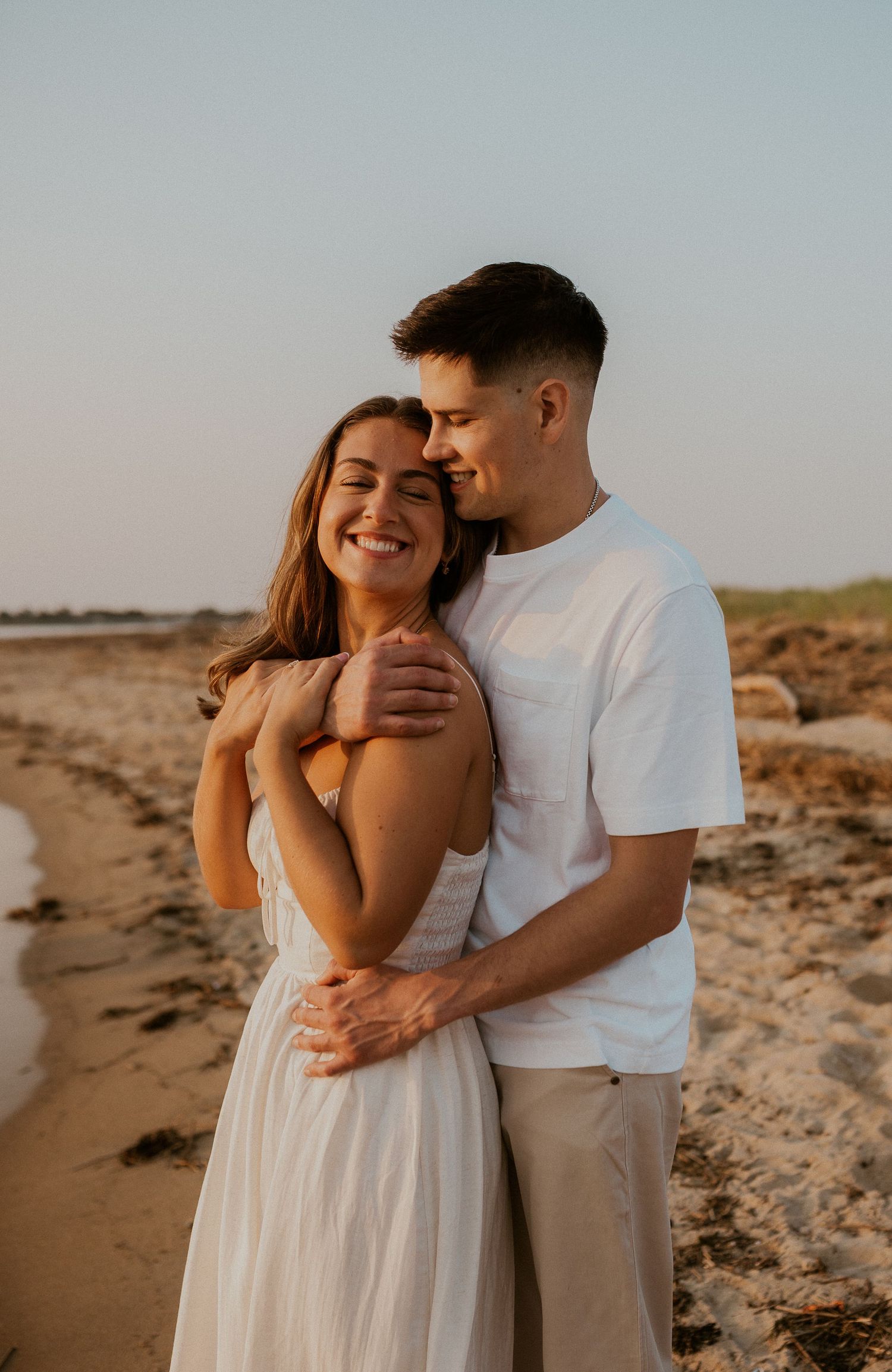 Couple embracing on beach during sunset wearing coordinated white outfits.