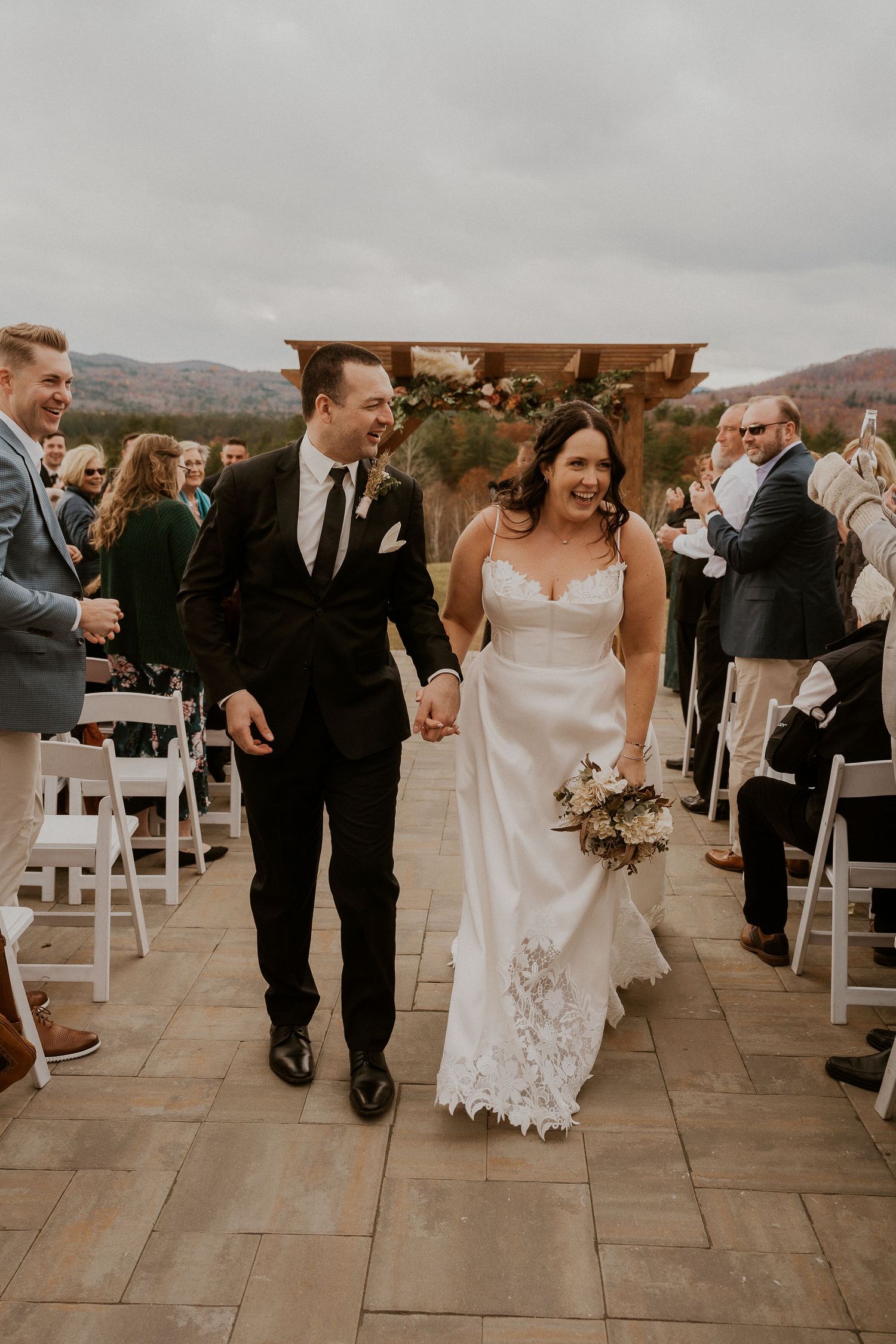 A joyful wedding recessional on a stone patio with guests celebrating on both sides.