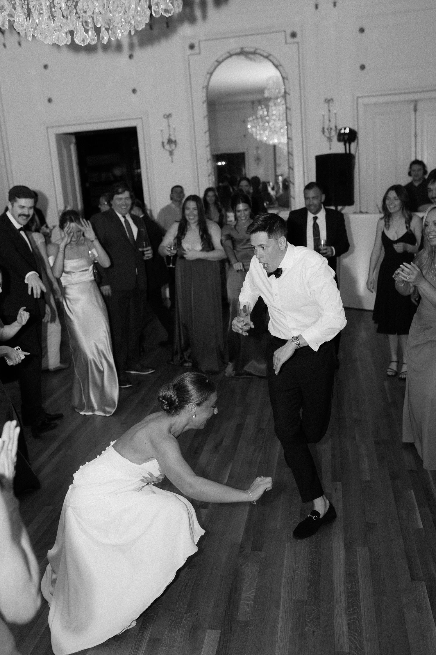 Bride and groom dancing energetically on the dance floor surrounded by guests at an elegant wedding reception.