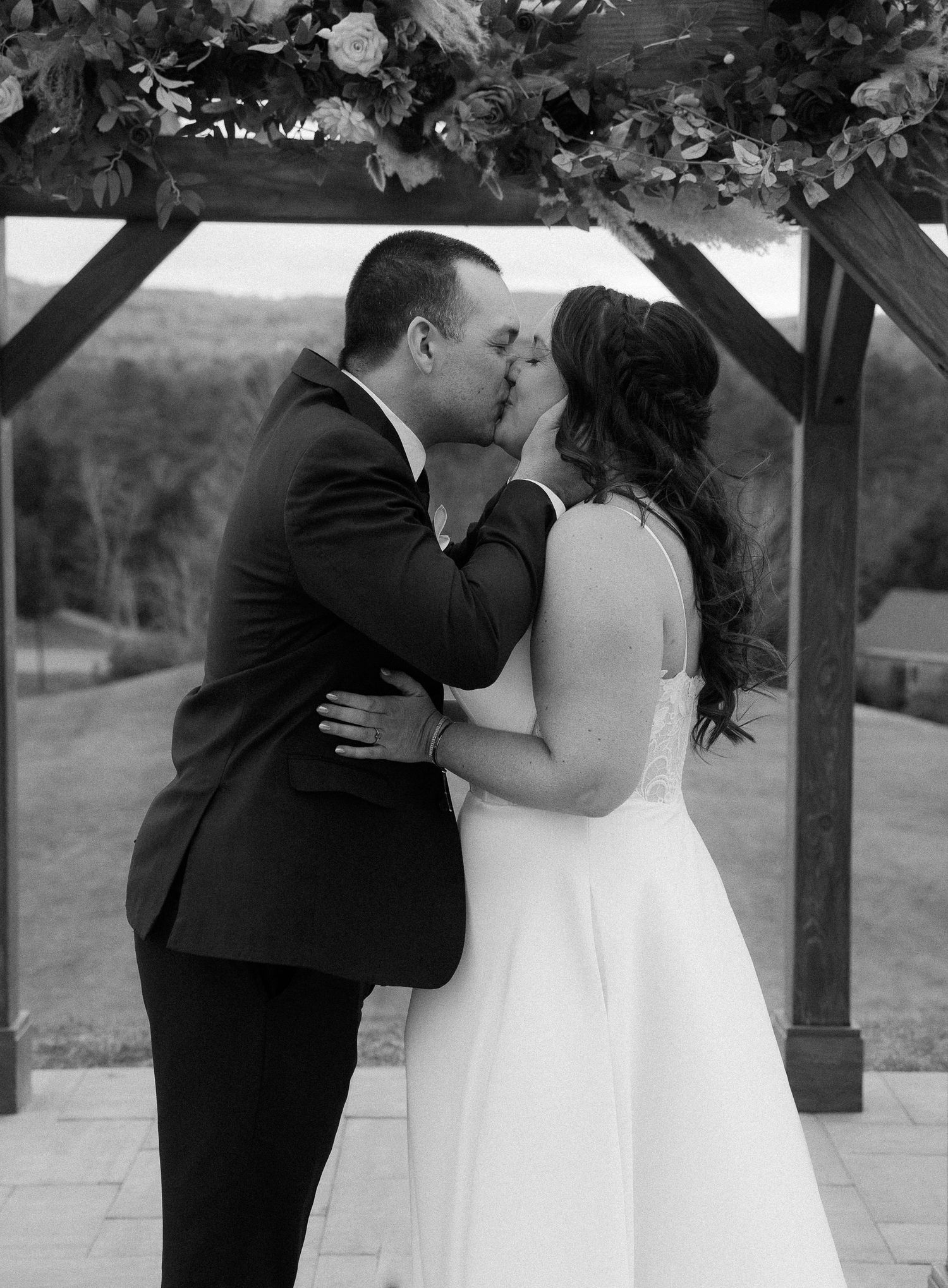 A black and white wedding photo capturing an intimate moment under a wooden arch.