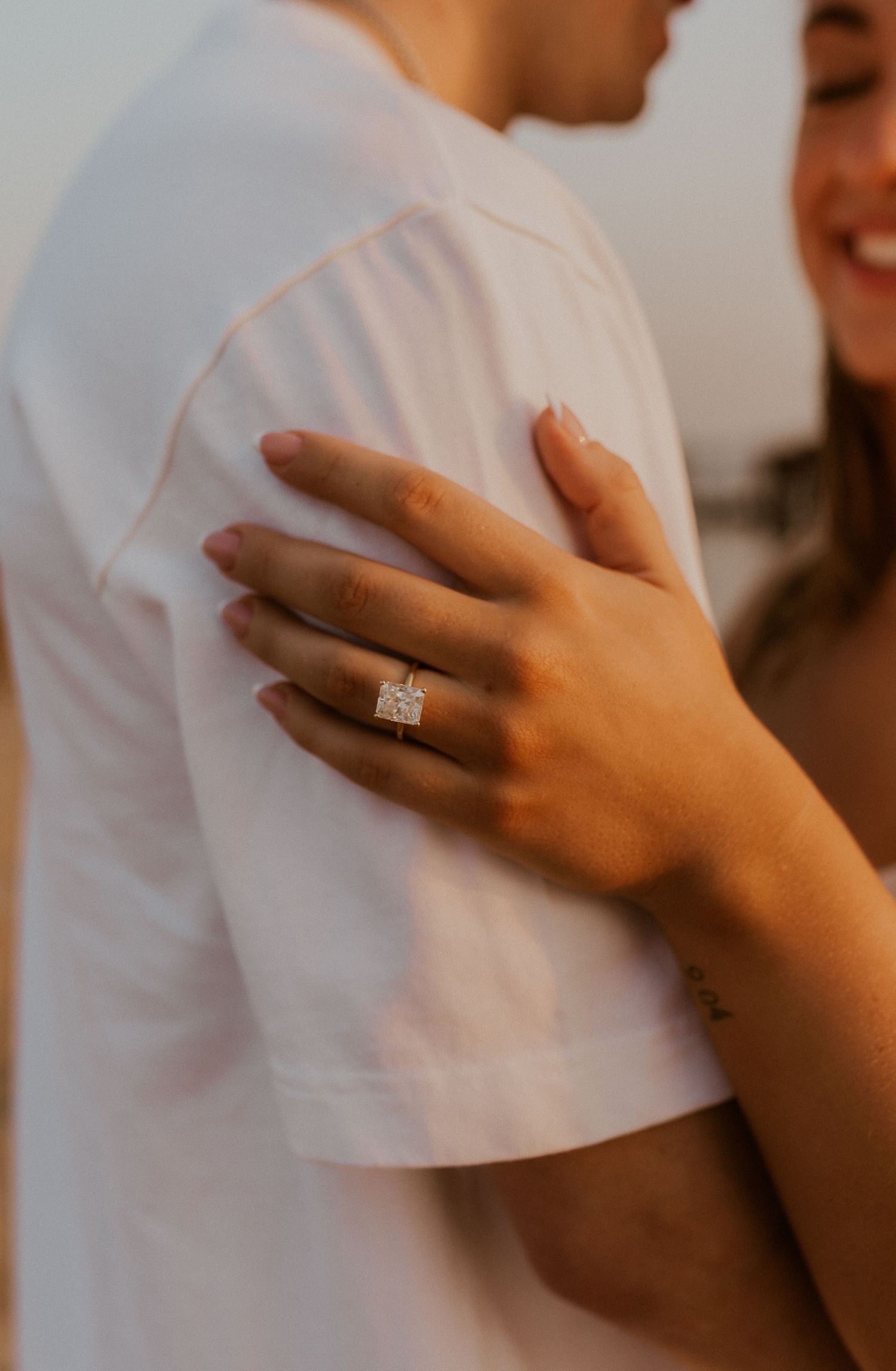 Close-up of a hand wearing an engagement ring resting on a white shirt sleeve.