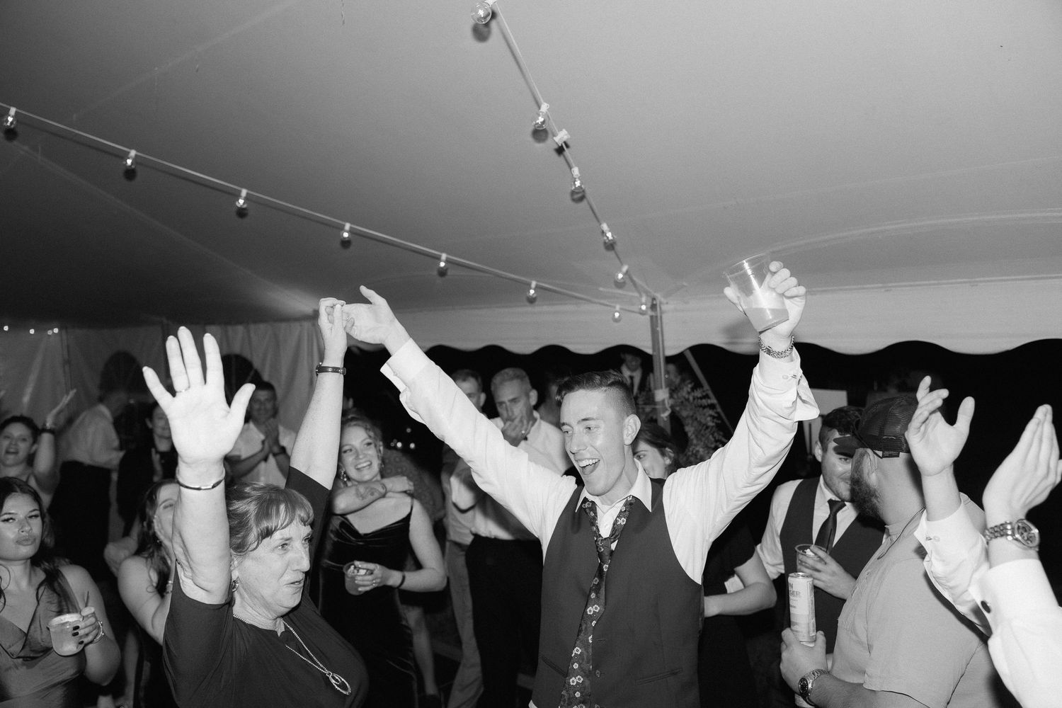 Wedding guests with raised arms dancing together under string lights.