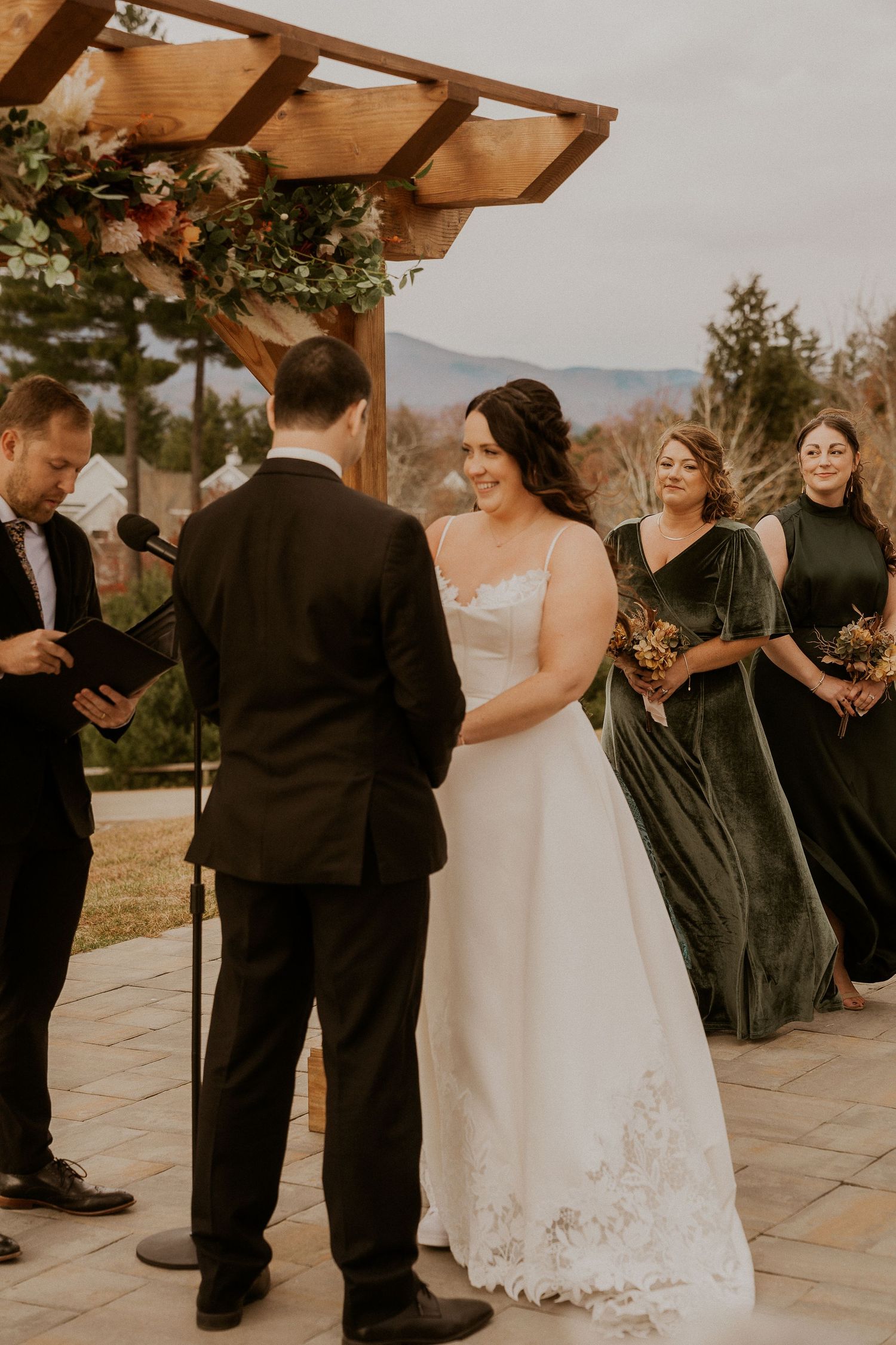 Wedding ceremony guests gathered under a wooden pergola during an outdoor celebration.