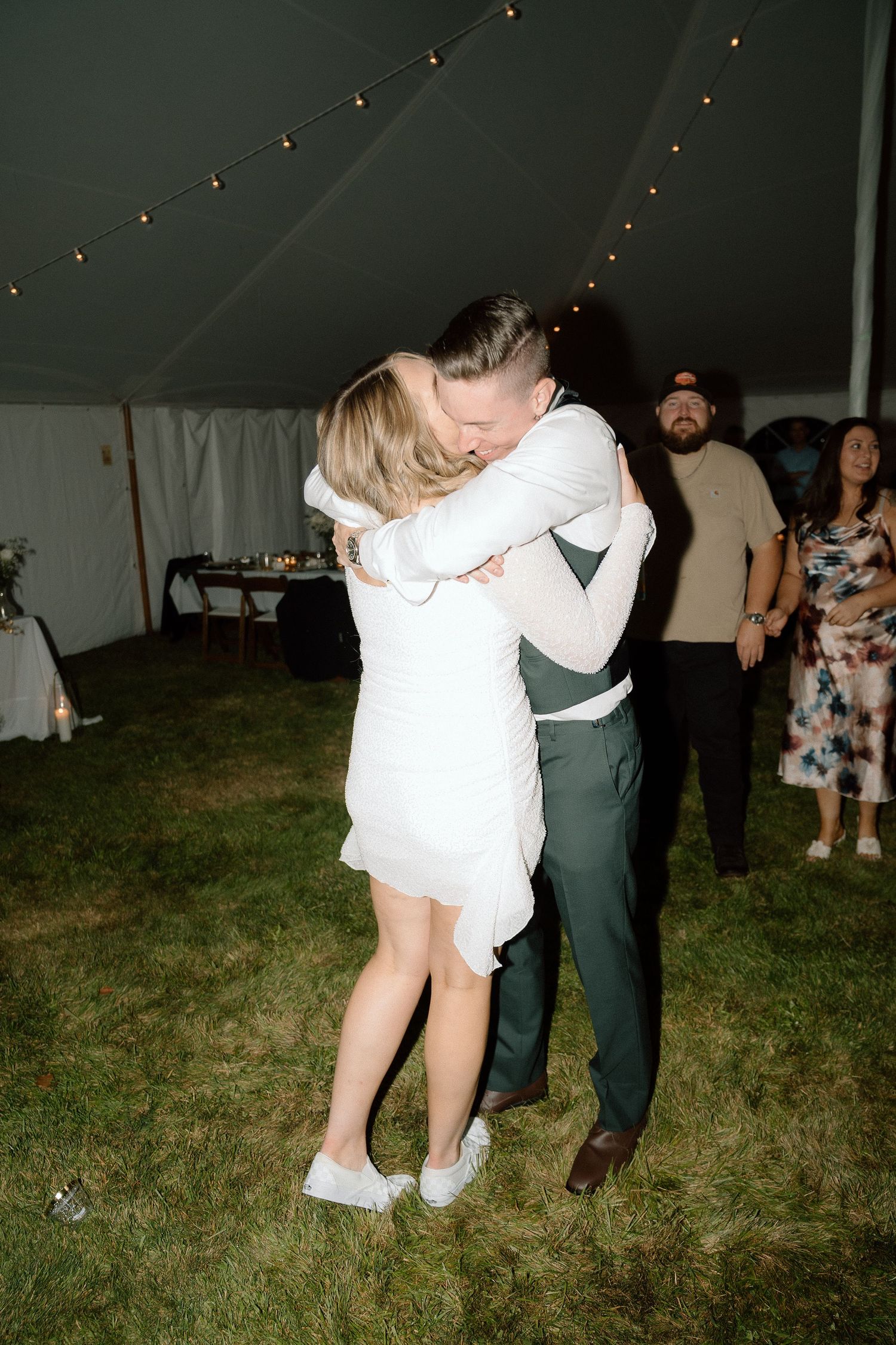 People dancing and celebrating at an outdoor evening wedding reception under a tent.