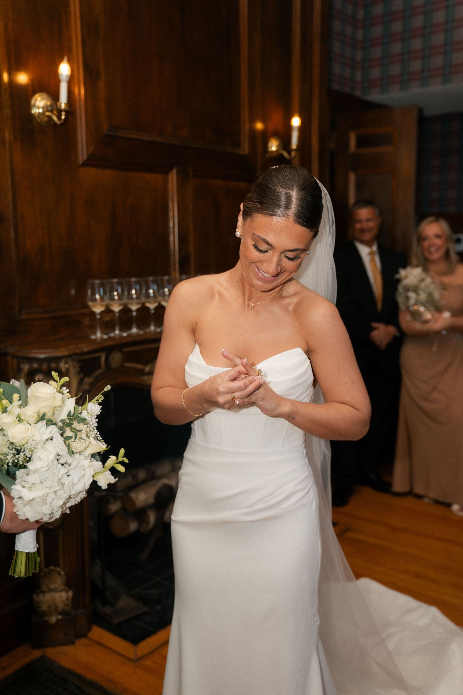 Elegant bride in strapless white gown admires her new wedding ring while holding a white floral bouquet.