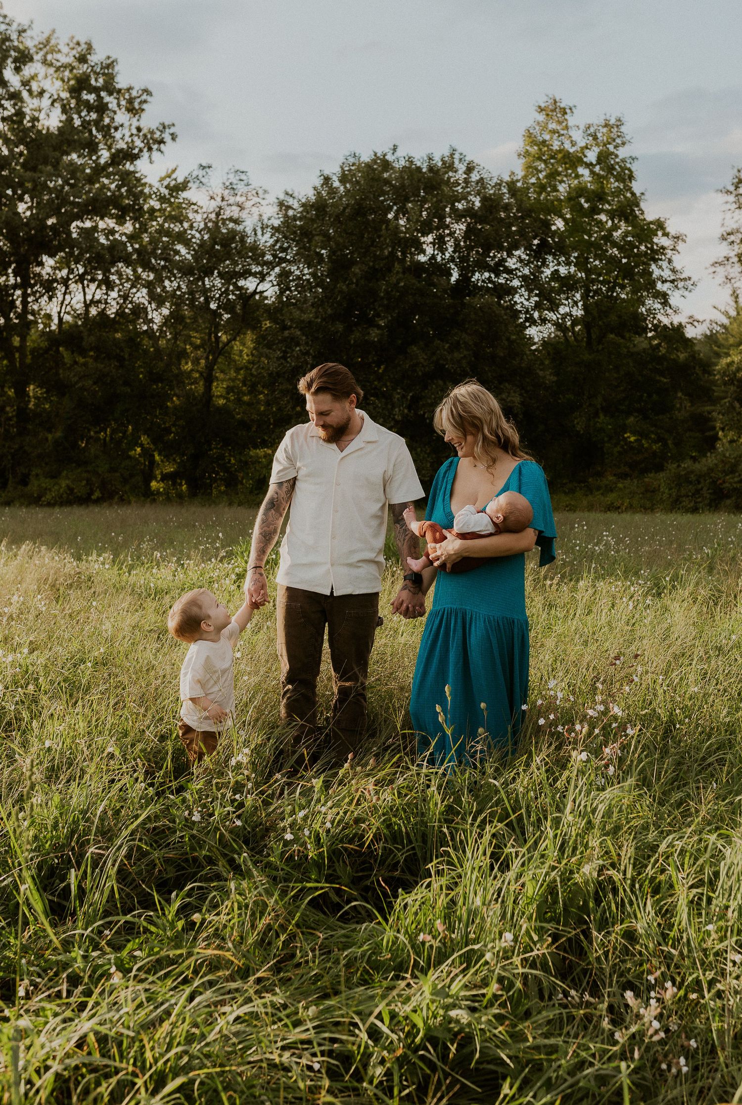 Family standing together in a tall grass field during golden hour.